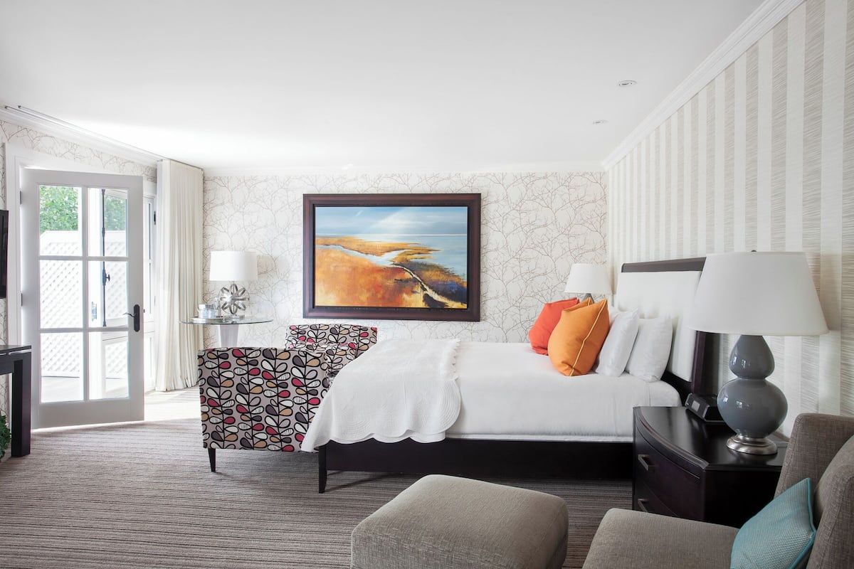 Quarto de hotel com cama, poltrona, escrivaninha e um quadro na parede.