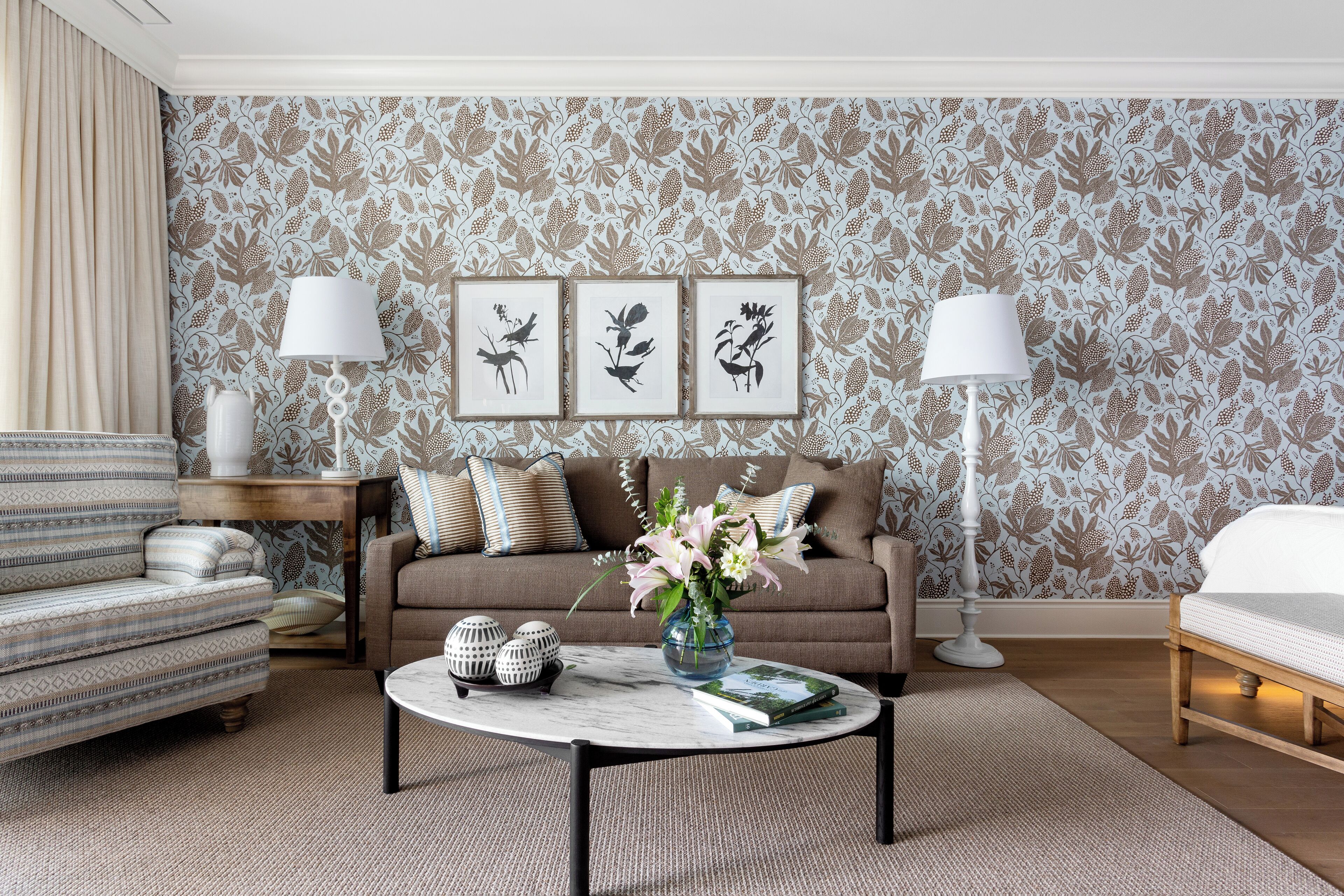 A living room with patterned wallpaper, a sofa, a coffee table with decorative items, and two lamps.