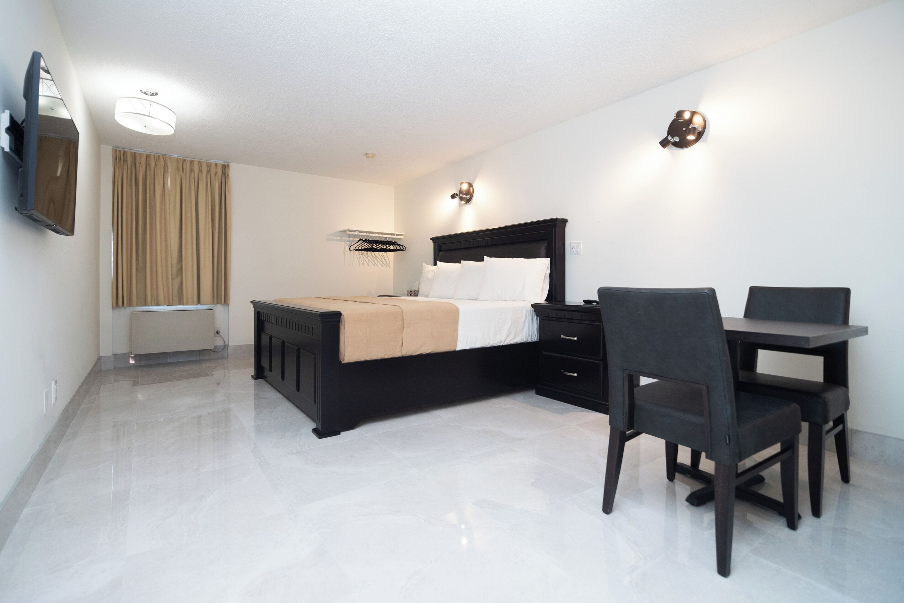 A modern hotel room with a bed, bedside table, chair, and a small desk area.