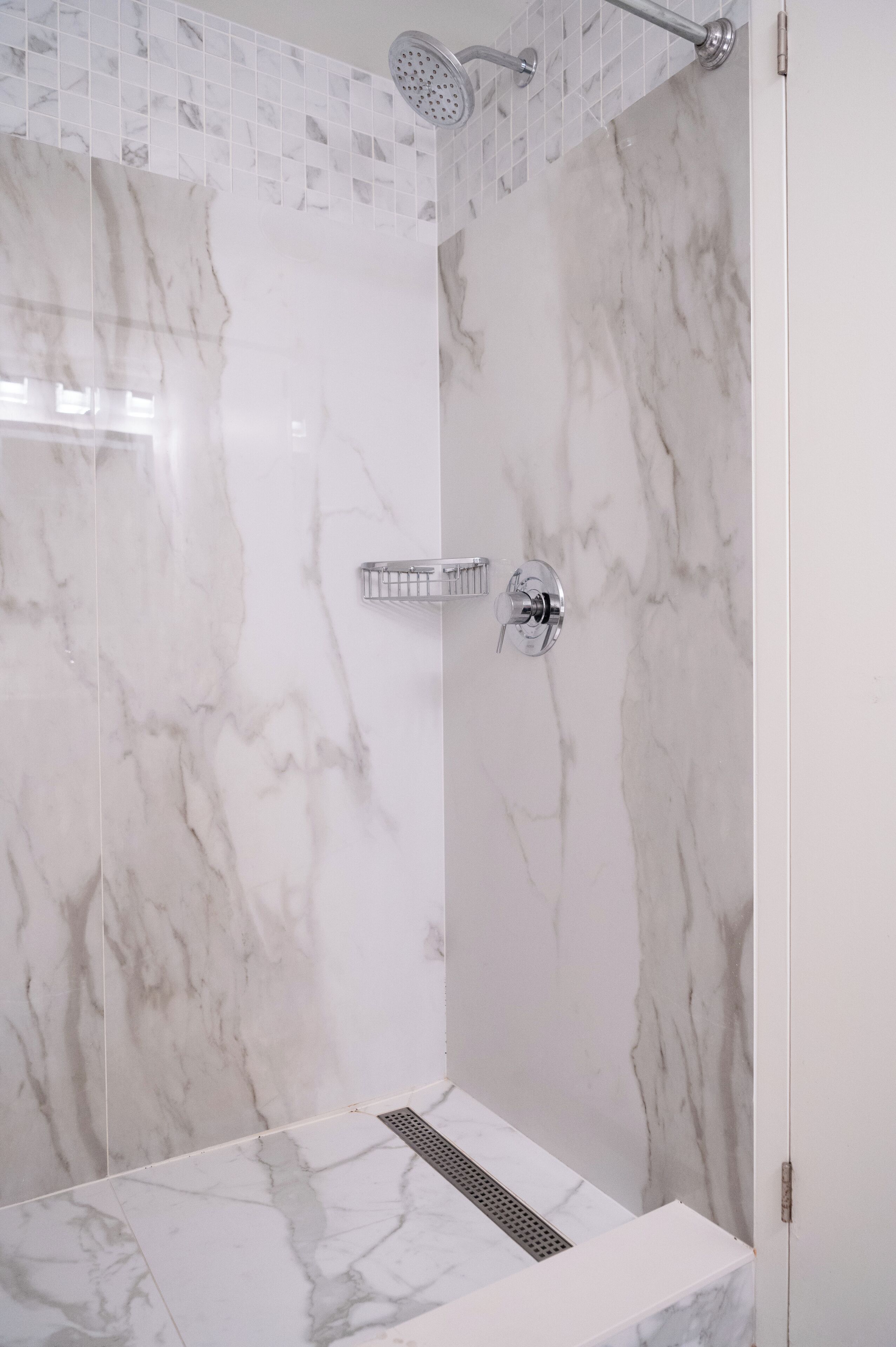 Eine Dusche mit Marmorwand, Brausekopf und Abfluss.