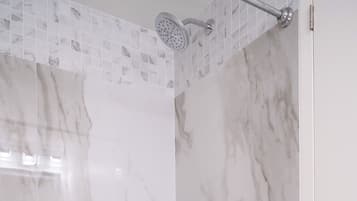 Eine Dusche mit Marmorwand, Brausekopf und Abfluss.
