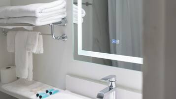 Un baño moderno con un lavabo blanco, un espejo grande y toallas blancas ordenadas.