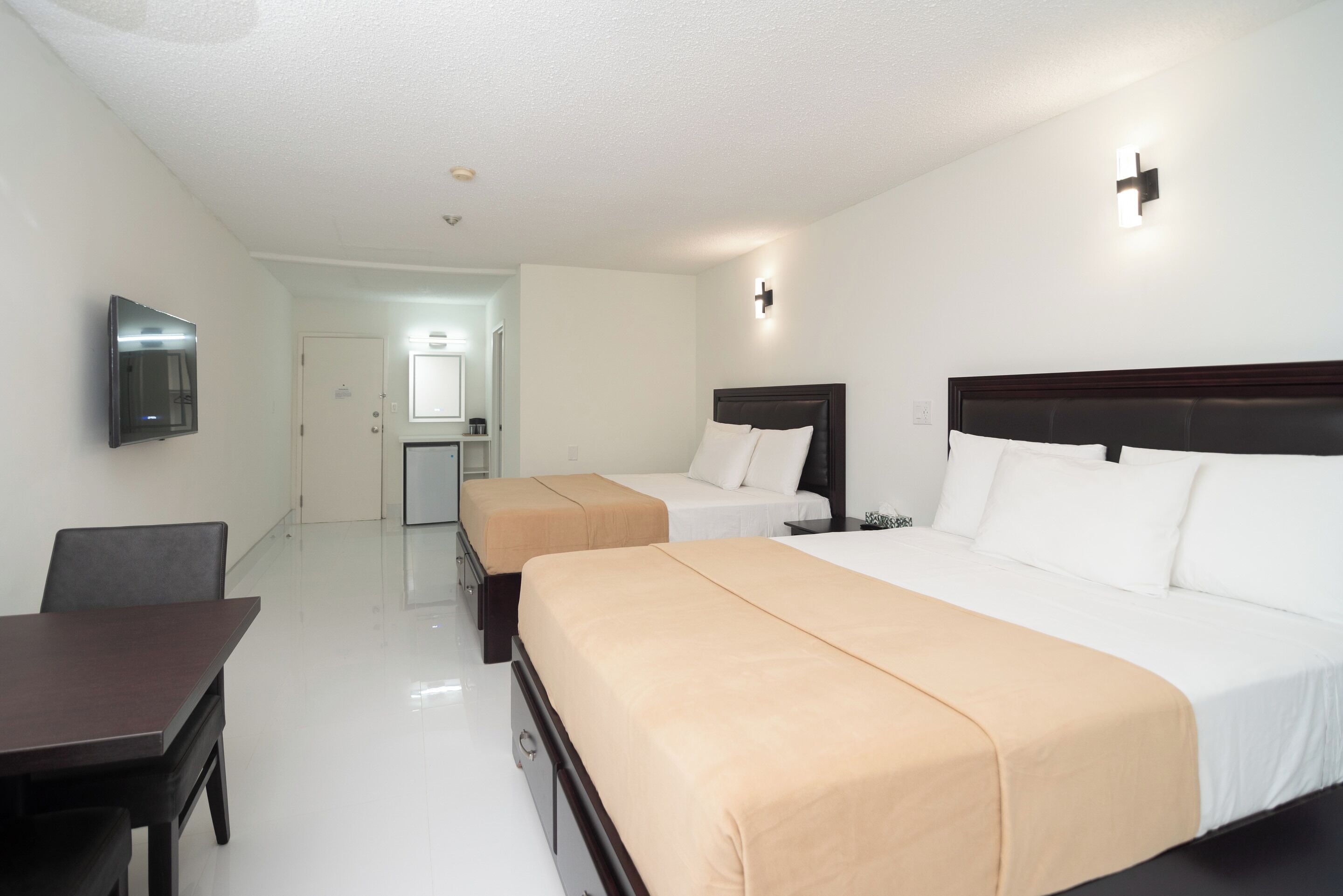 Quarto de hotel com duas camas, uma escrivaninha, uma cadeira, televisão e uma pequena cozinha.