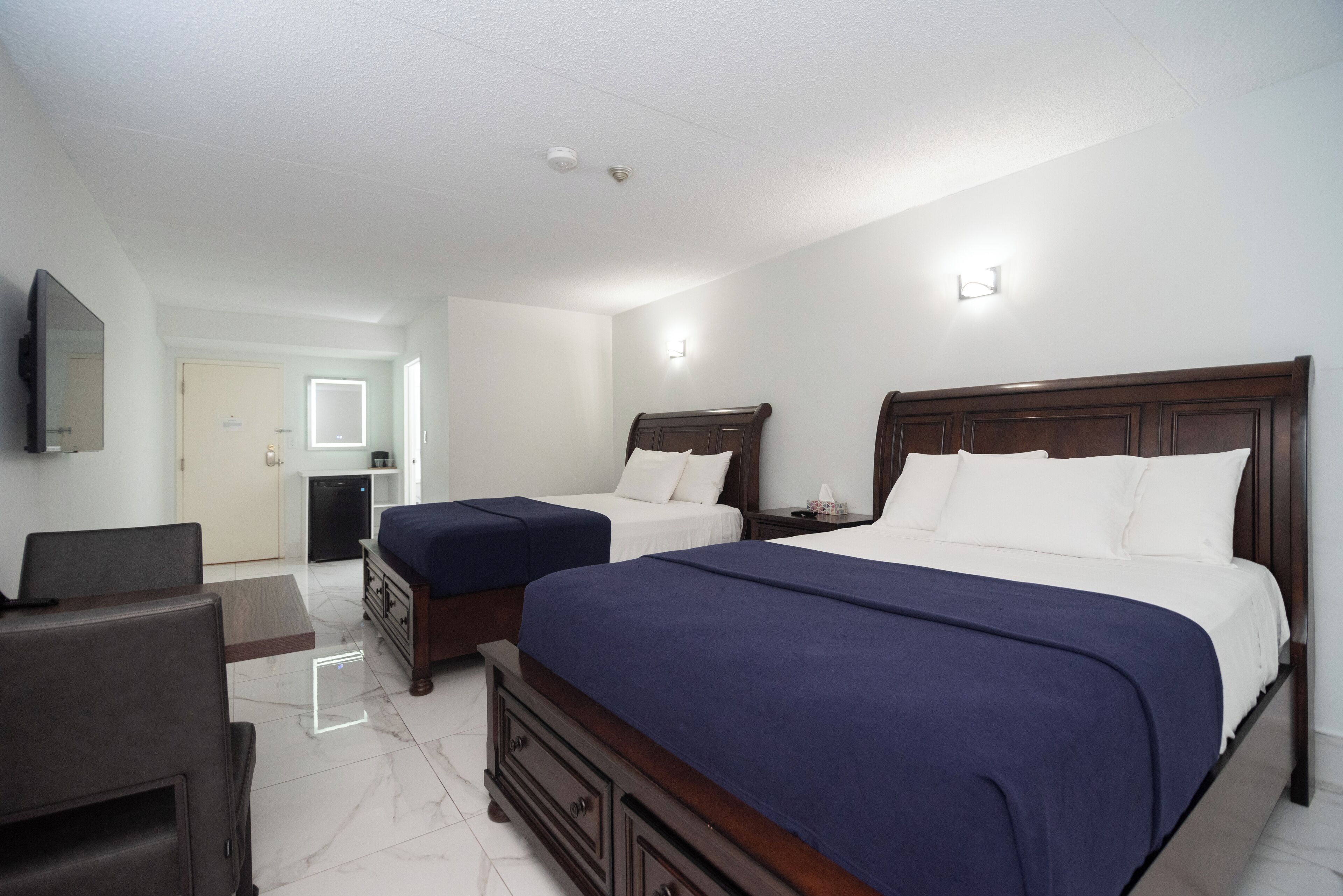 A hotel room with two beds, a TV, a desk, and a mirror.