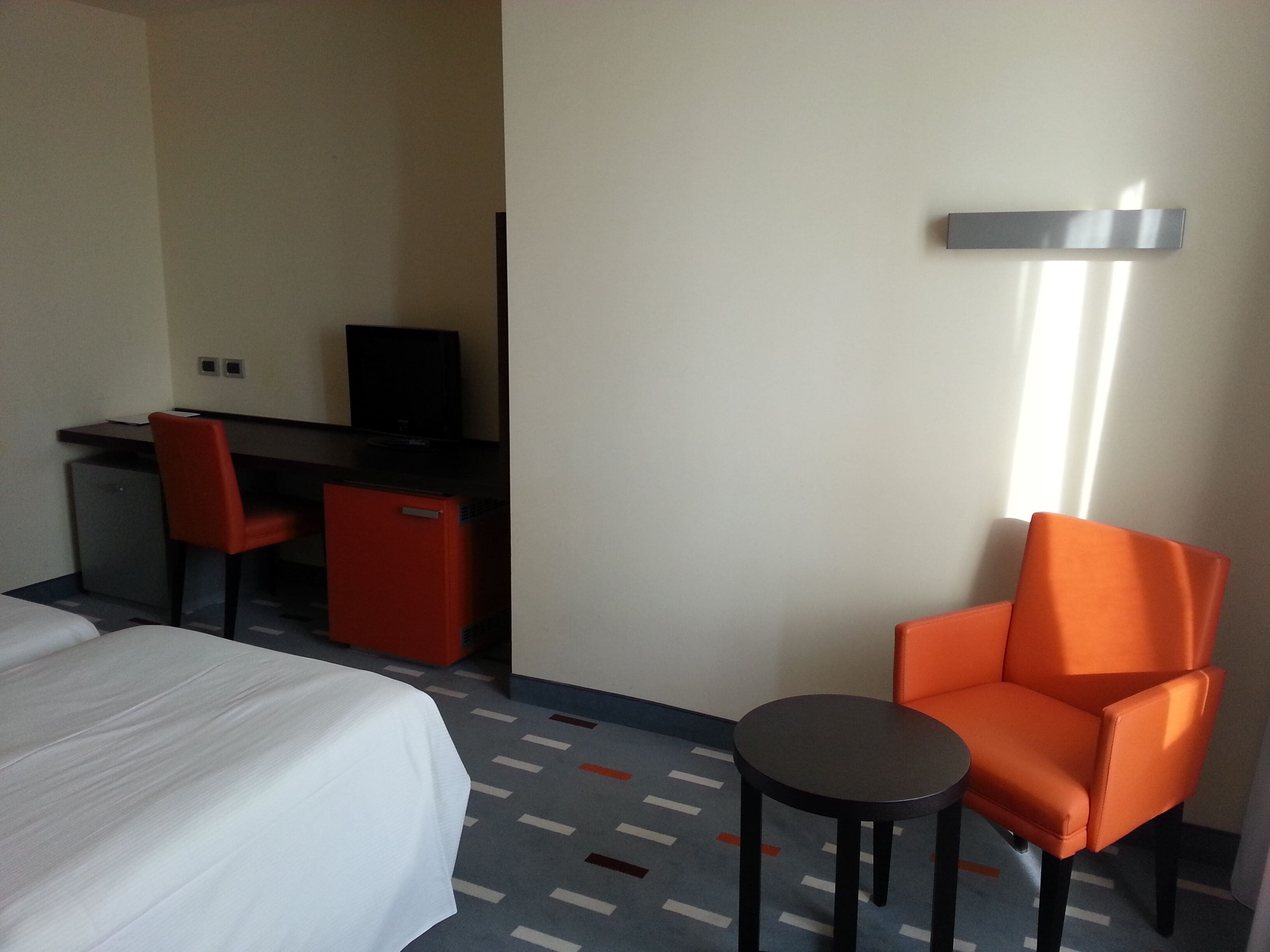 Una camera d'hotel con un letto, una scrivania con un computer, un tavolino e una sedia arancione.