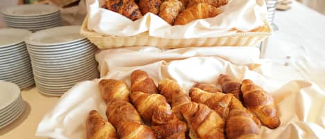 A table with baskets of croissants and stacks of plates.