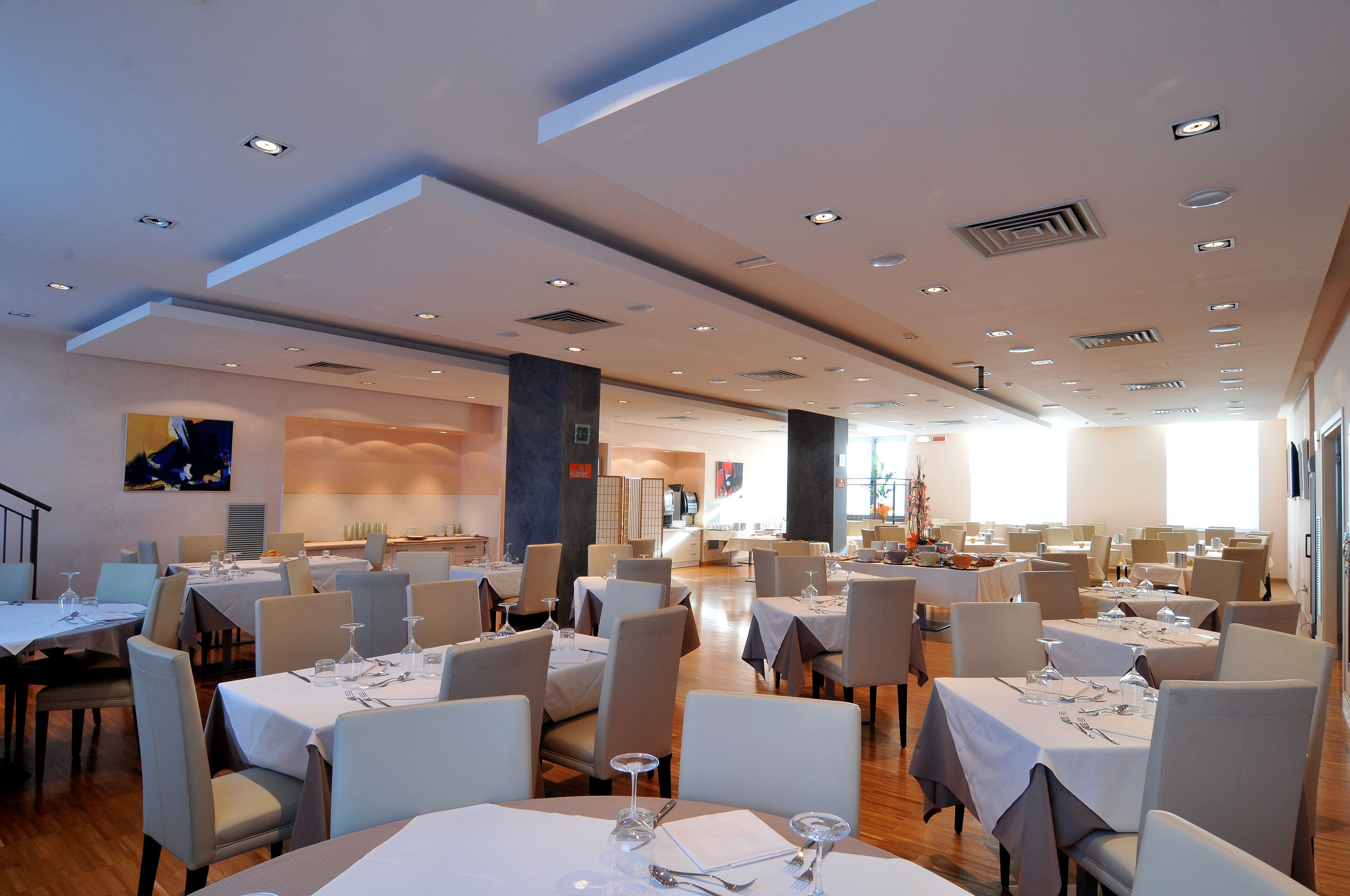 A spacious dining area with multiple tables and chairs, ceiling lights, and a modern interior design.