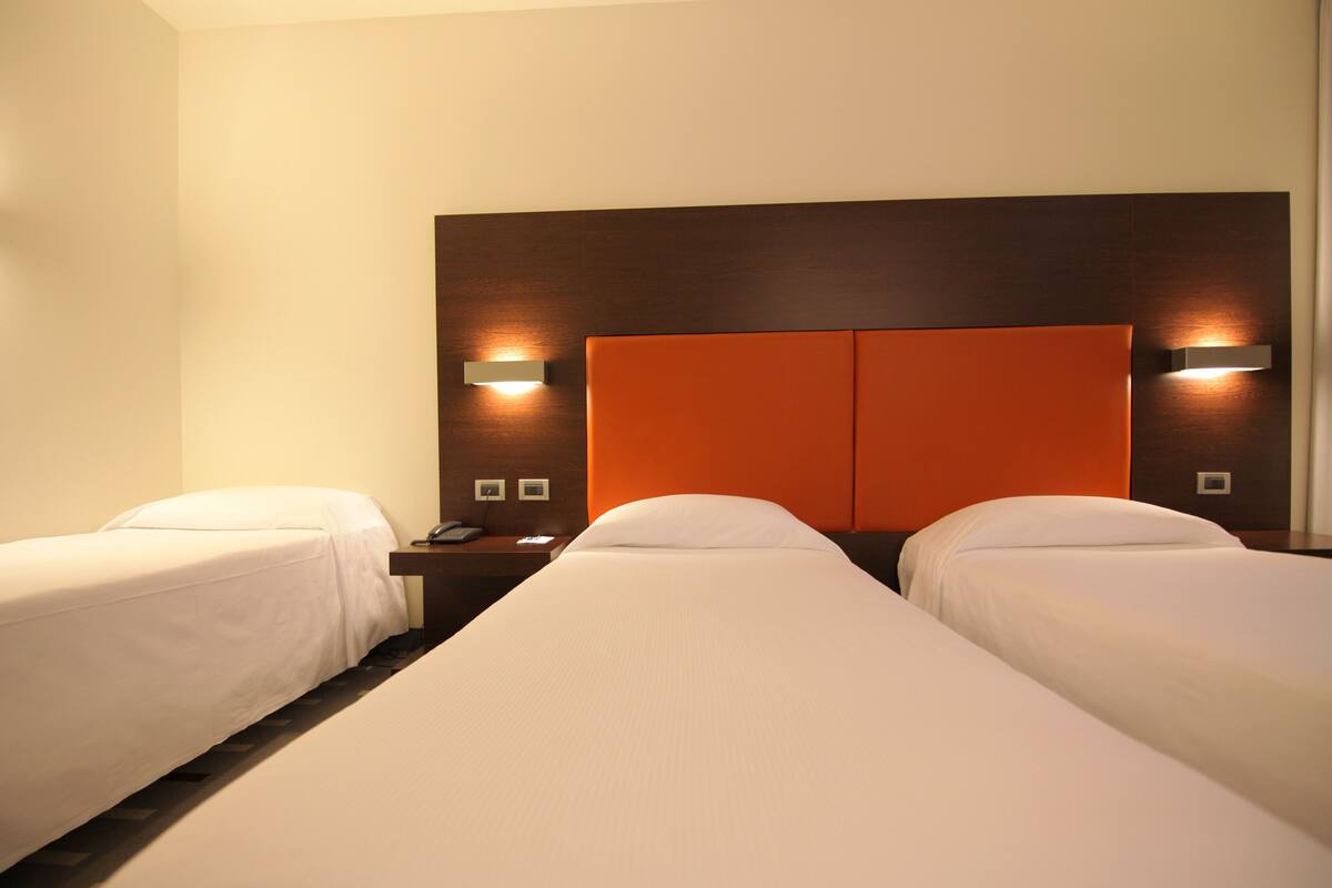 Habitación de hotel con dos camas individuales, cabecero de madera y lámparas de noche.