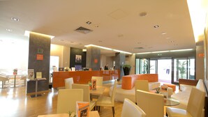 Un moderno vestíbulo de hotel con una recepción, zonas de estar y grandes ventanales.