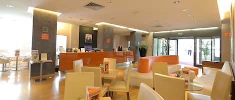 A modern hotel lobby with a reception desk, seating areas, and large windows.