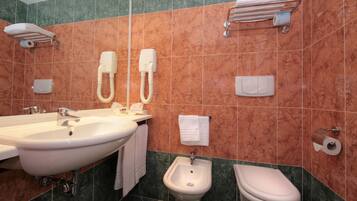 A bathroom with a sink, bidet, toilet, towel rack, and towel dispenser.