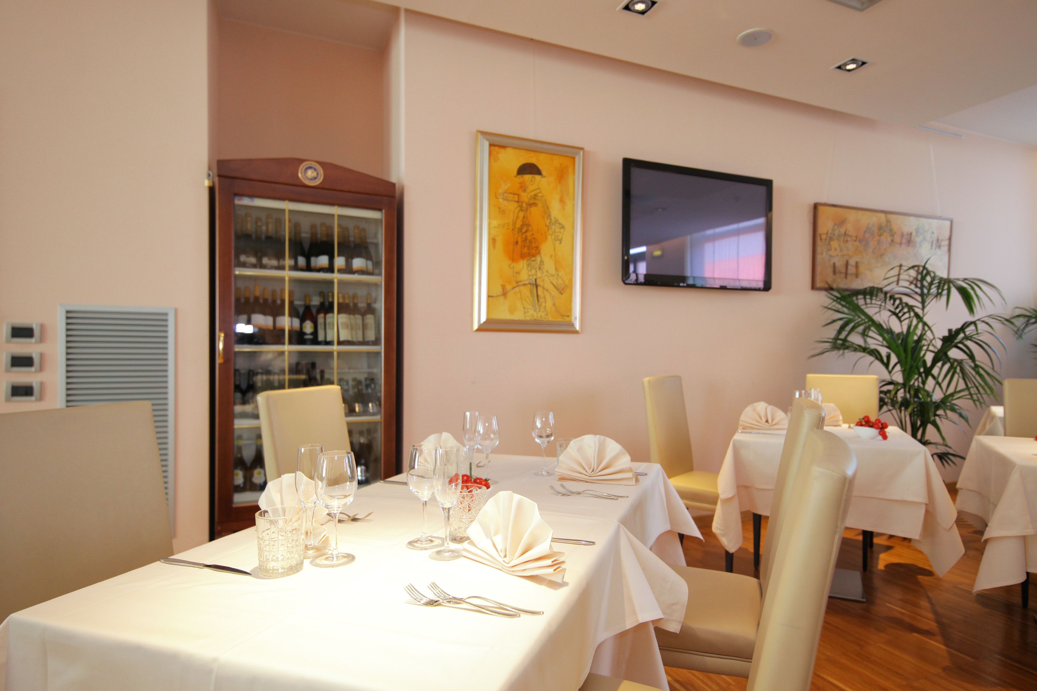 A dining area with tables set for a meal, a wine cooler, and artwork on the walls.