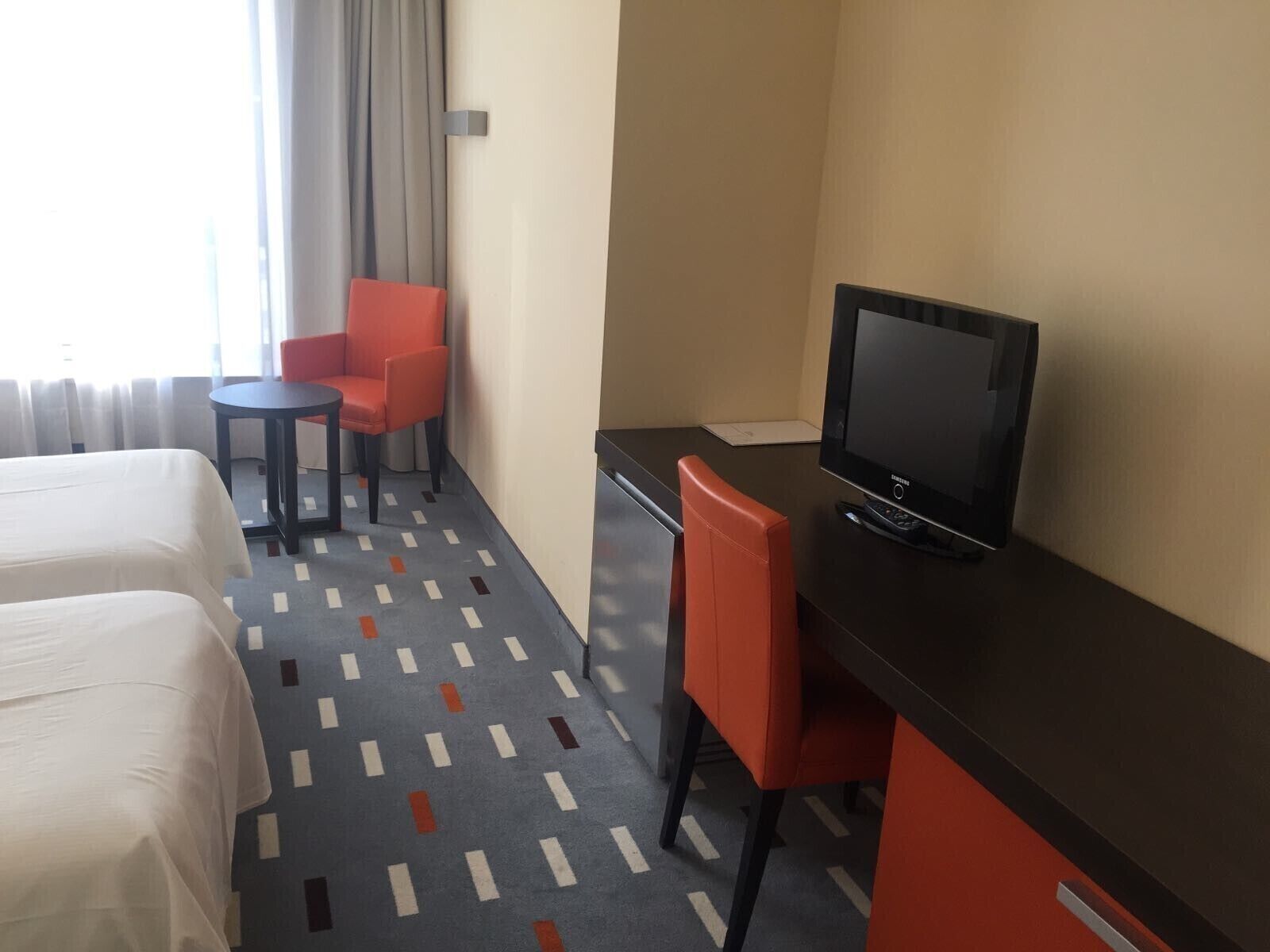 A hotel room with two beds, a desk with a TV, a small table, and two chairs.