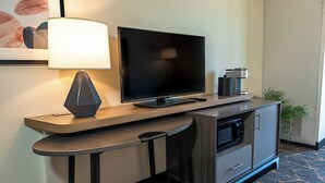 A modern hotel room with a flat-screen TV, a lamp, a microwave, and a small cabinet. - Holiday Inn & Suites Oakland Airport by IHG (Oakland)