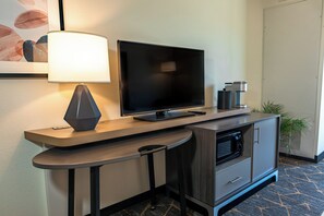 Ein modernes Hotelzimmer mit Flachbildfernseher, einer Lampe, einer Mikrowelle und einem kleinen Schrank.