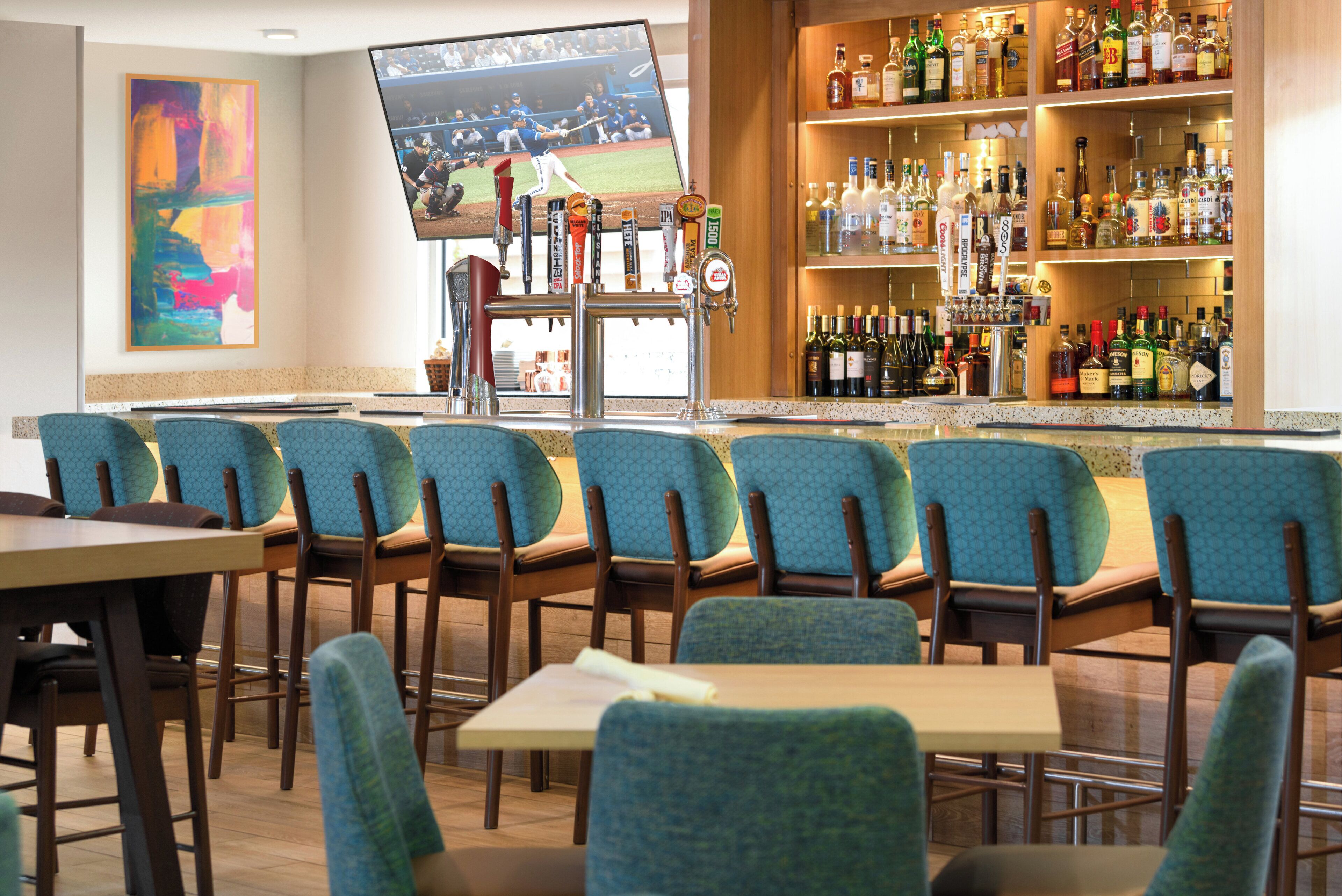 A bar area with multiple seating options and a television screen displaying a sports event.