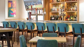 A bar area with multiple seating options and a television screen displaying a sports event.