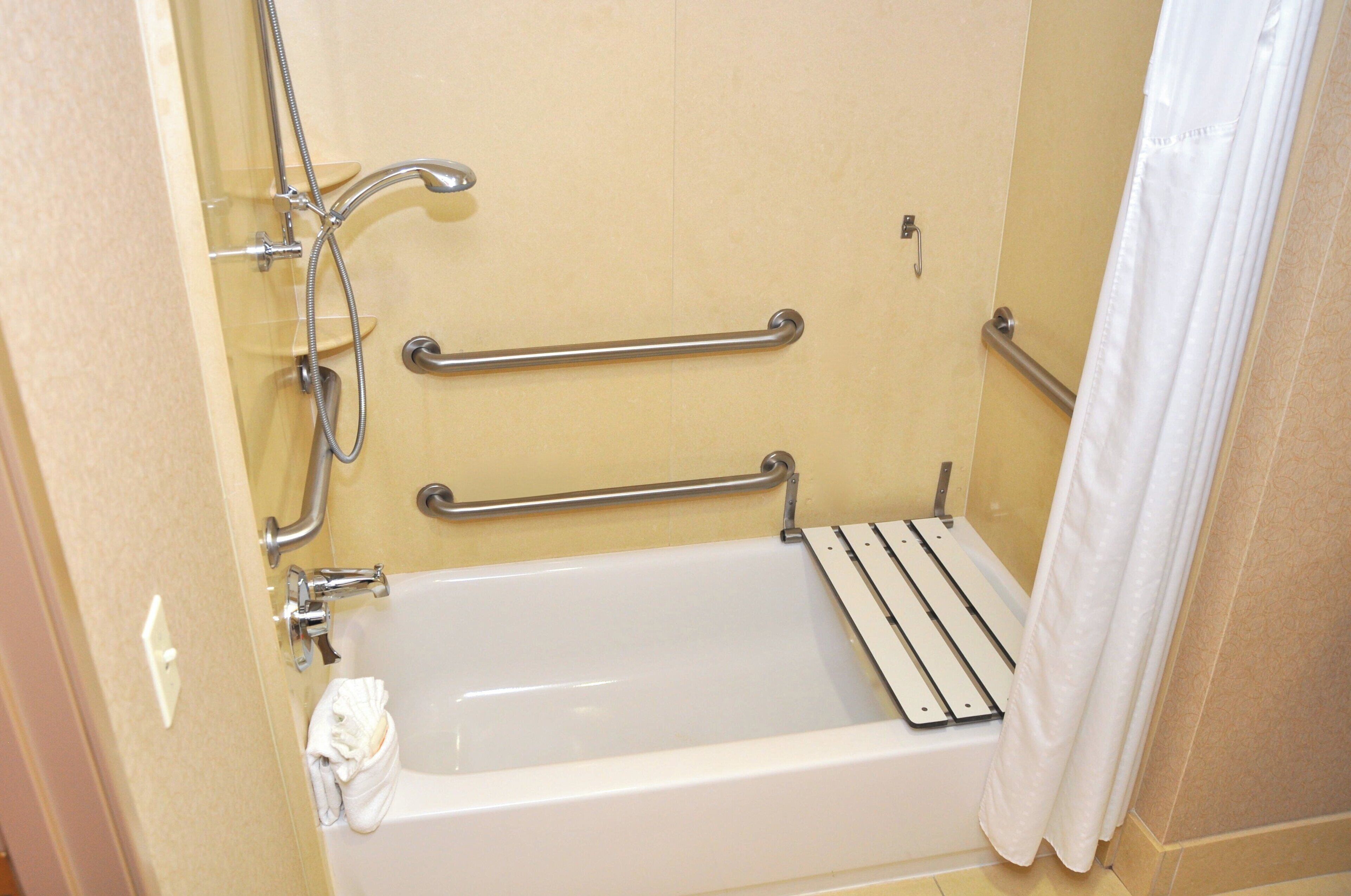 A bathroom with a bathtub, grab bars, and a shower head.