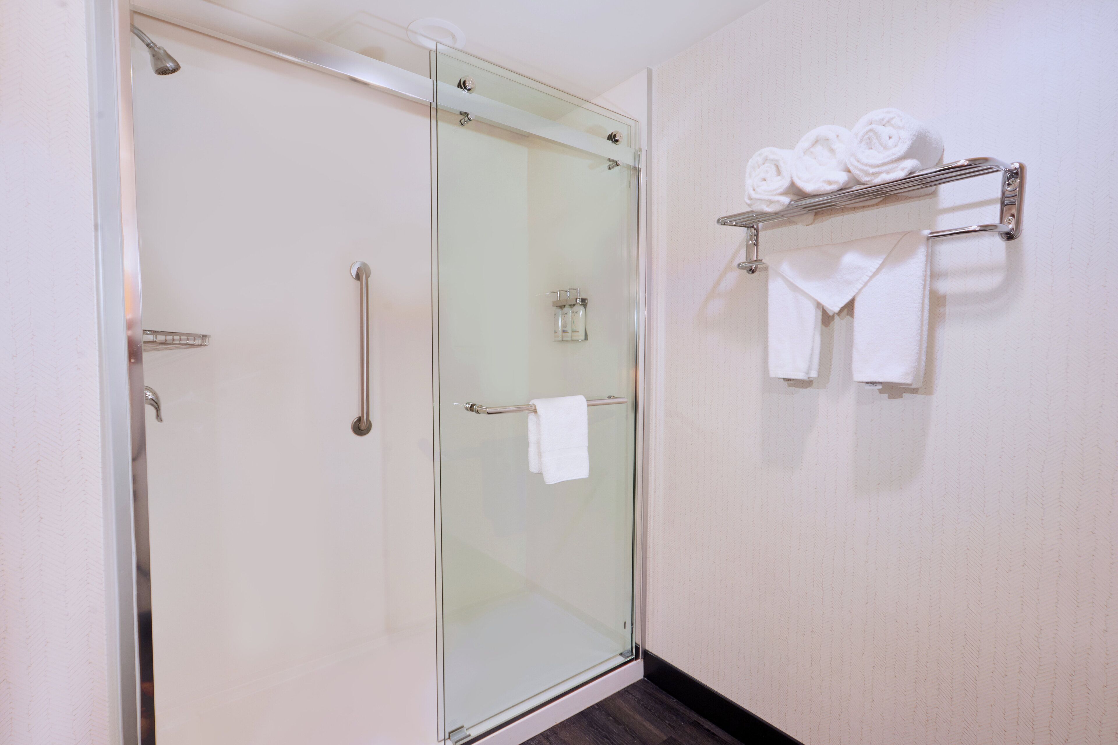 A glass-enclosed shower with a towel rack holding rolled towels.