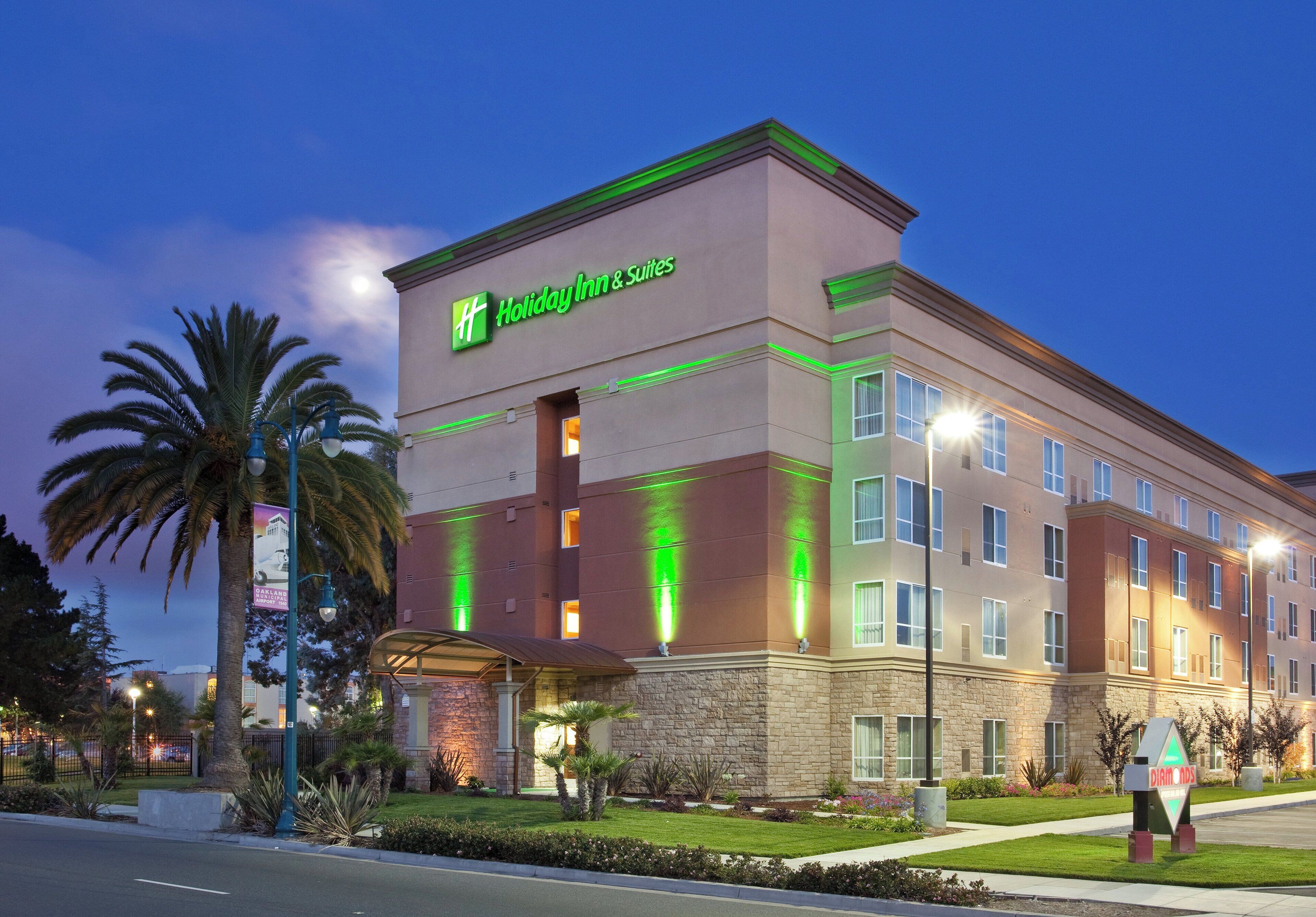 A Holiday Inn & Suites hotel with a stone facade, multiple windows, and a green neon sign.