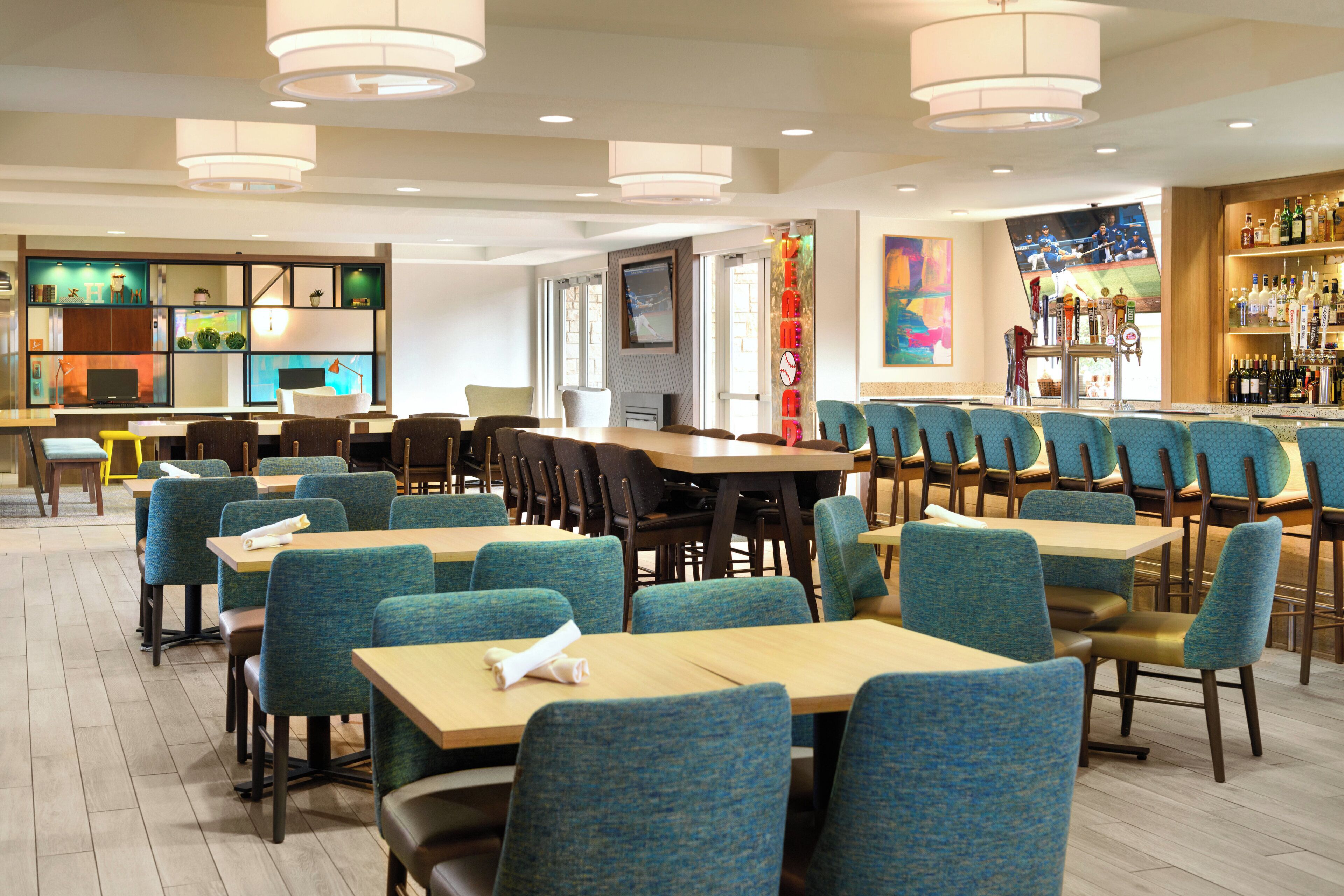 A restaurant with multiple tables and chairs, a bar area, and a television screen.
