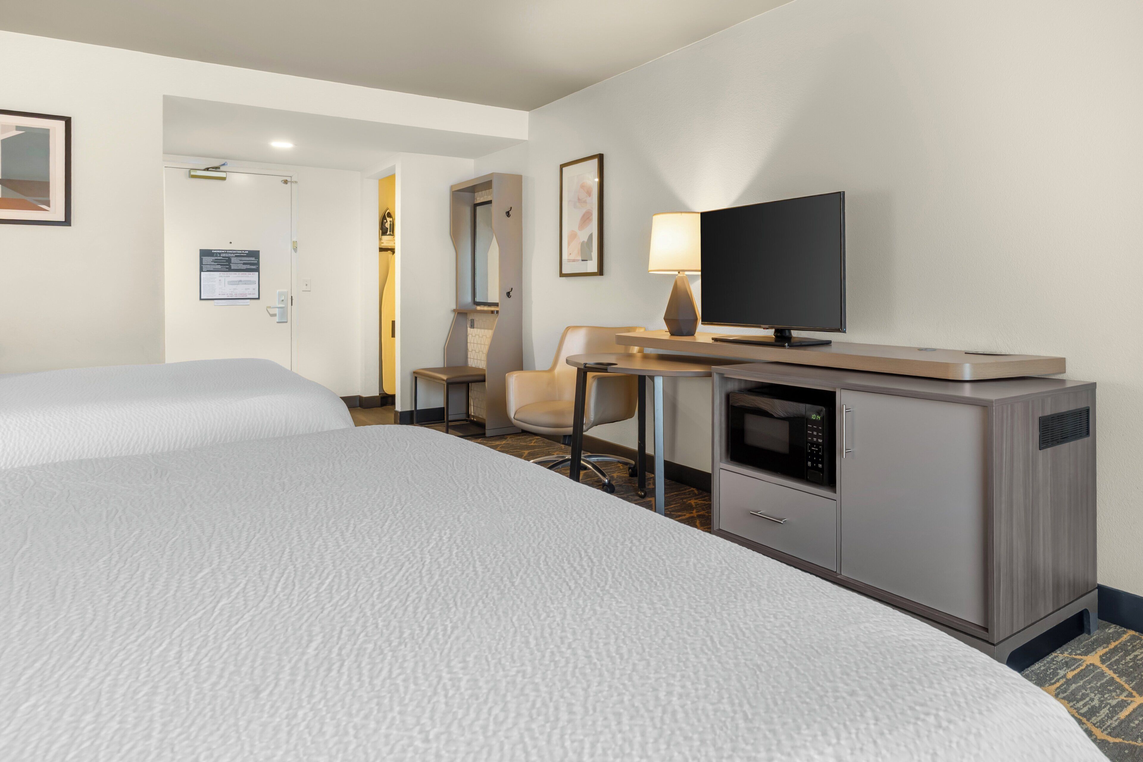 A hotel room with two beds, a desk with a flat-screen TV, a microwave, and a small seating area.