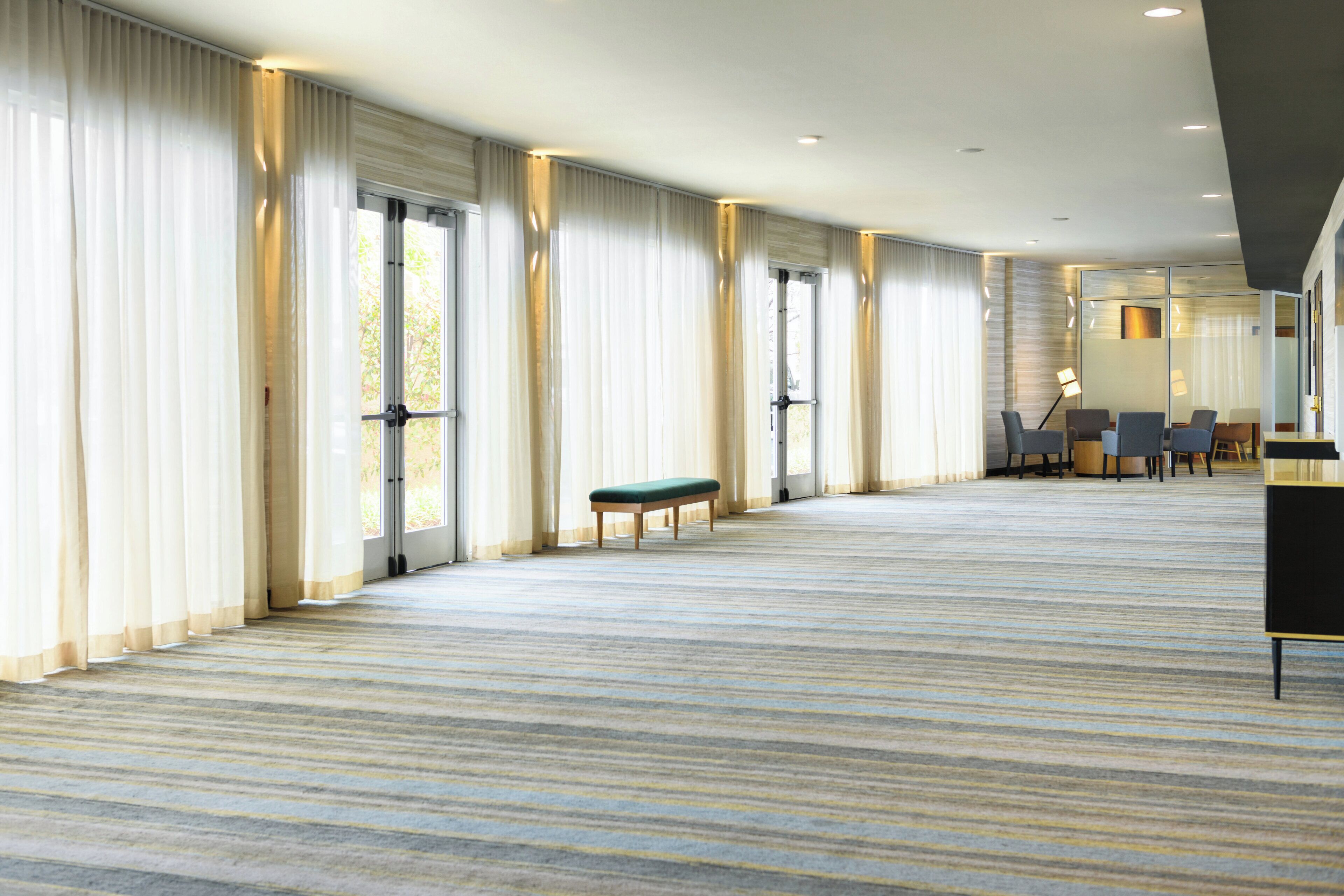 A spacious hotel room with large windows, a bench, and a seating area with tables and chairs.