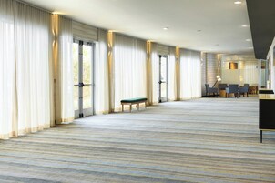 Una habitación de hotel amplia con ventanas grandes, un banco y una zona de estar con mesas y sillas.