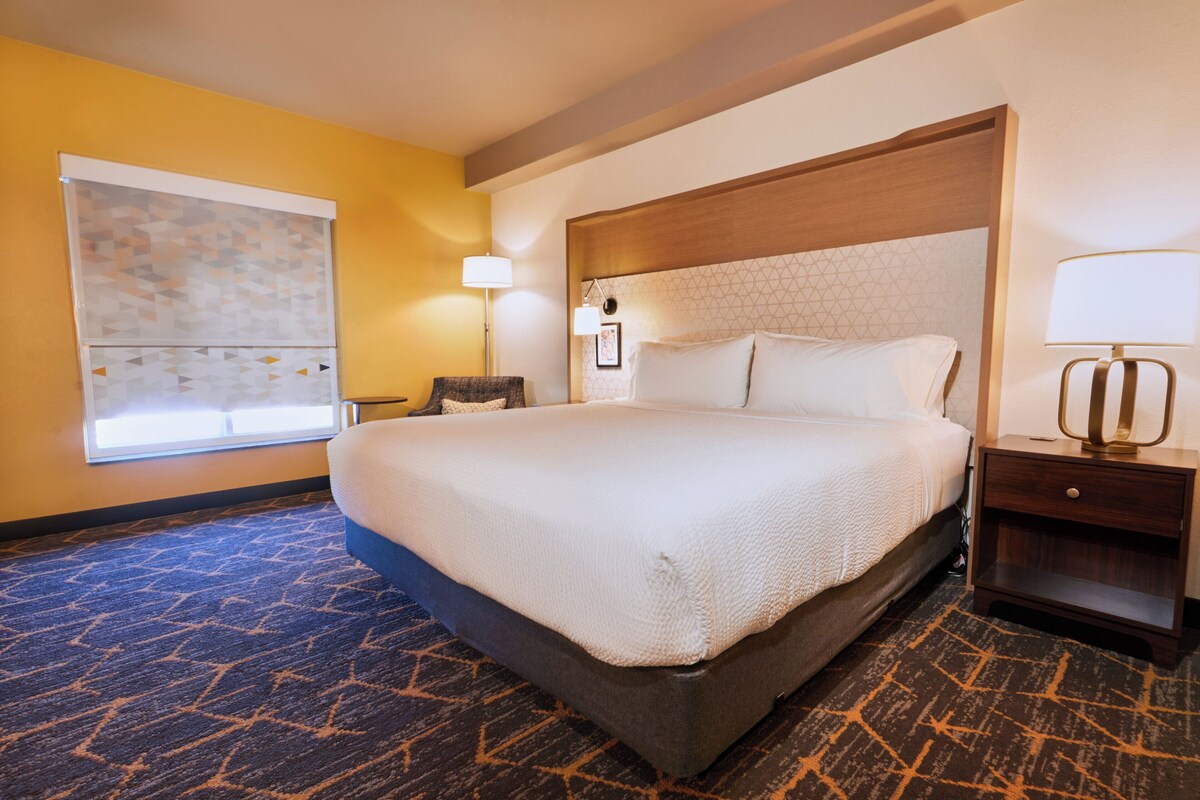 A hotel room with a large bed, a nightstand, a lamp, and a painting on the wall.