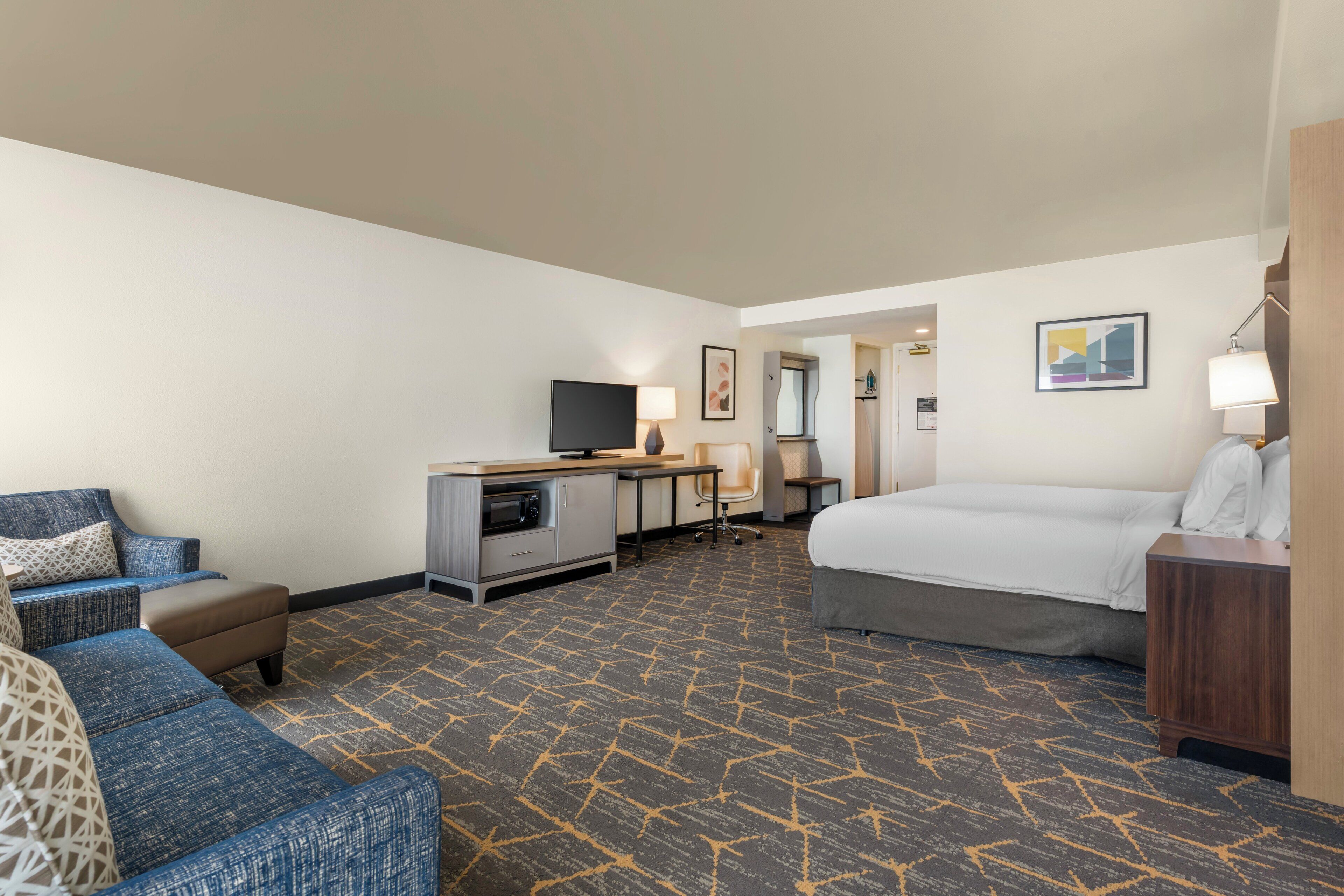 A hotel room with a bed, a desk with a computer, a television, and a seating area with a sofa and armchair.