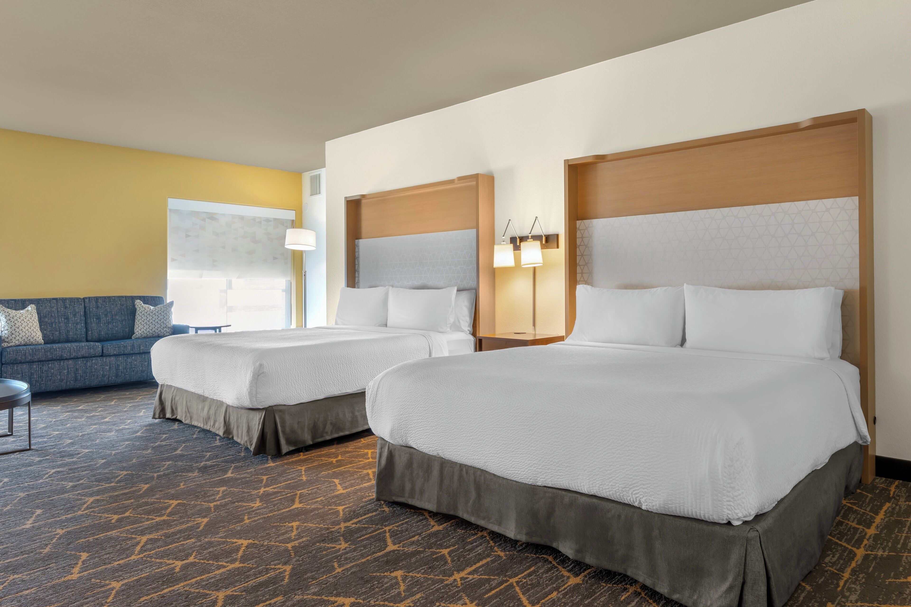 Una habitación de hotel con dos camas, un sofá y una lámpara.