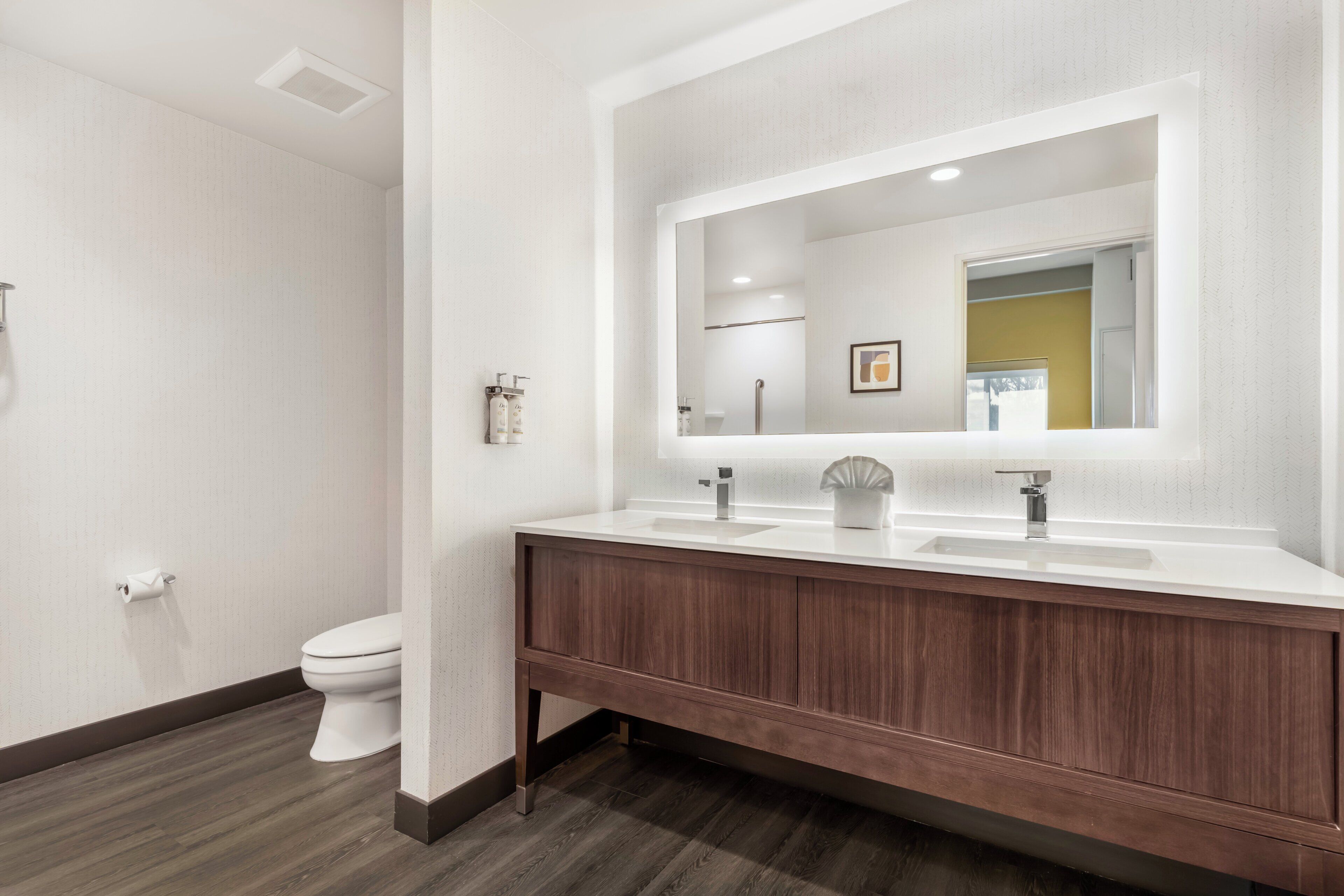 A modern bathroom with a wooden vanity, a large mirror, and a toilet.
