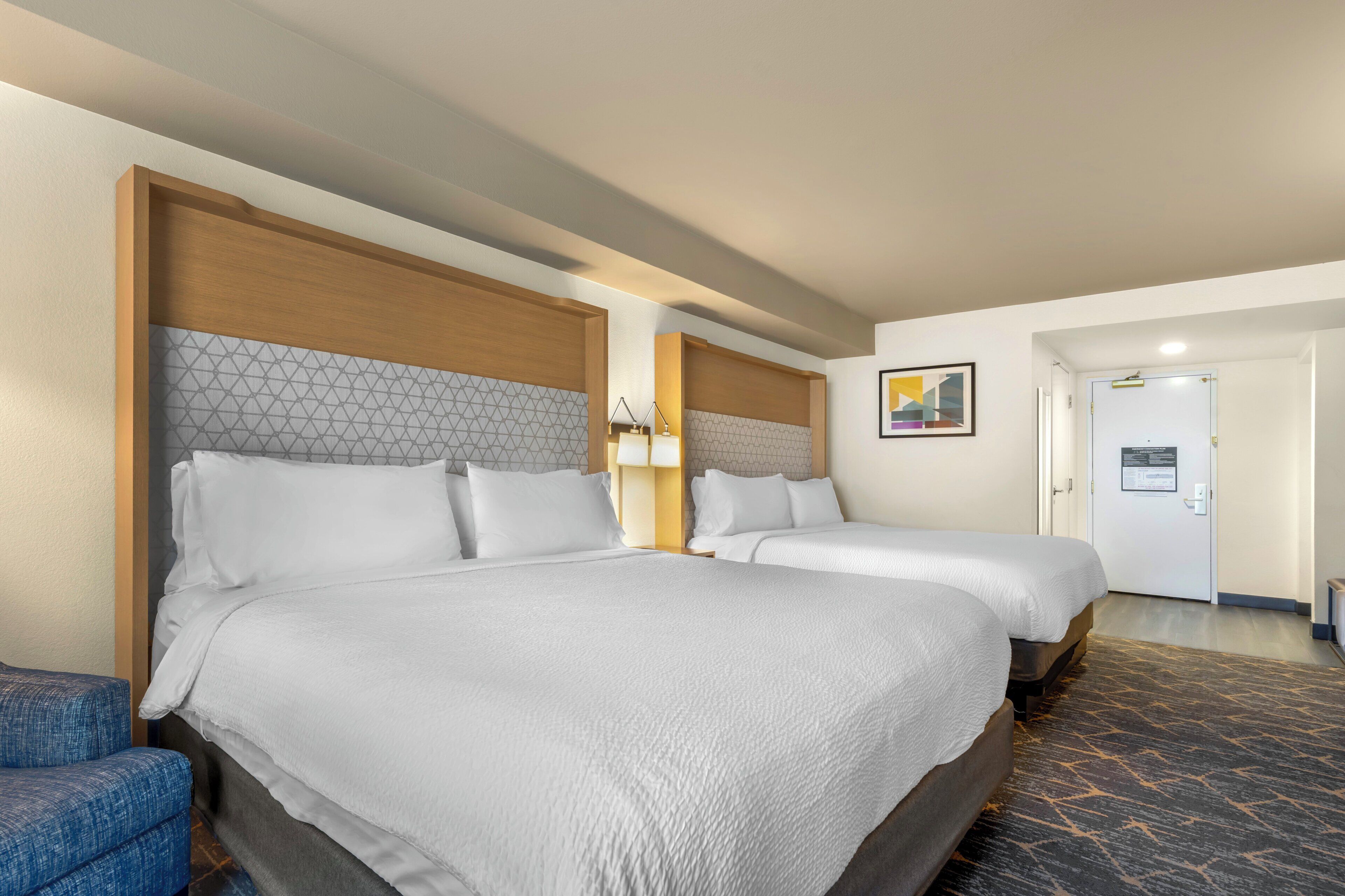 A hotel room with two beds, a desk, a chair, and a door.