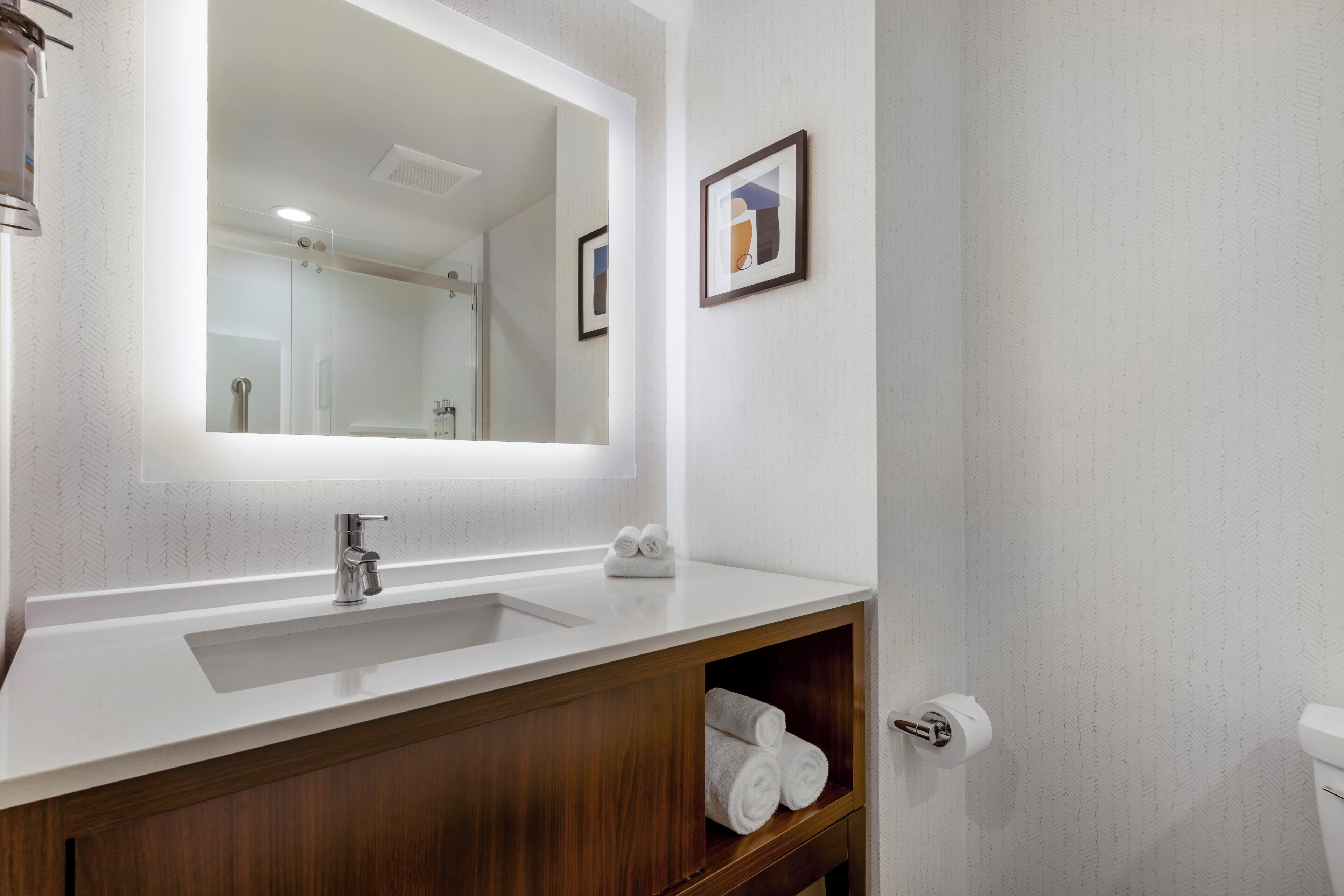 A bathroom with a large mirror, a sink, a wooden cabinet, and a toilet.