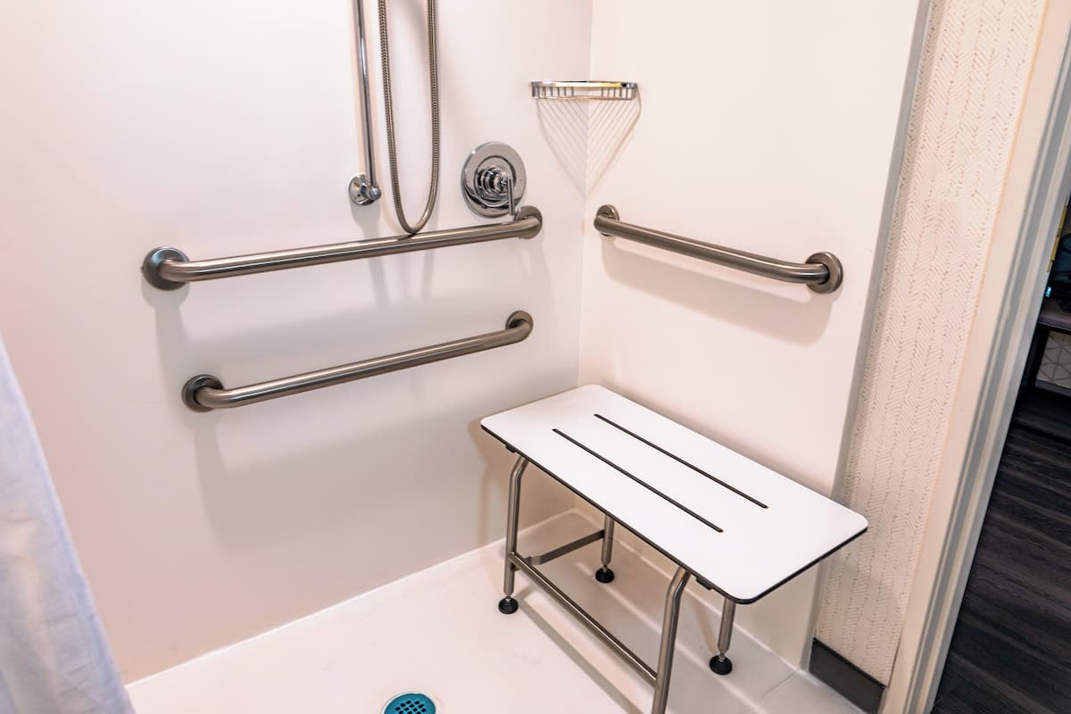 A bathroom with grab bars, a showerhead, and a white sink.