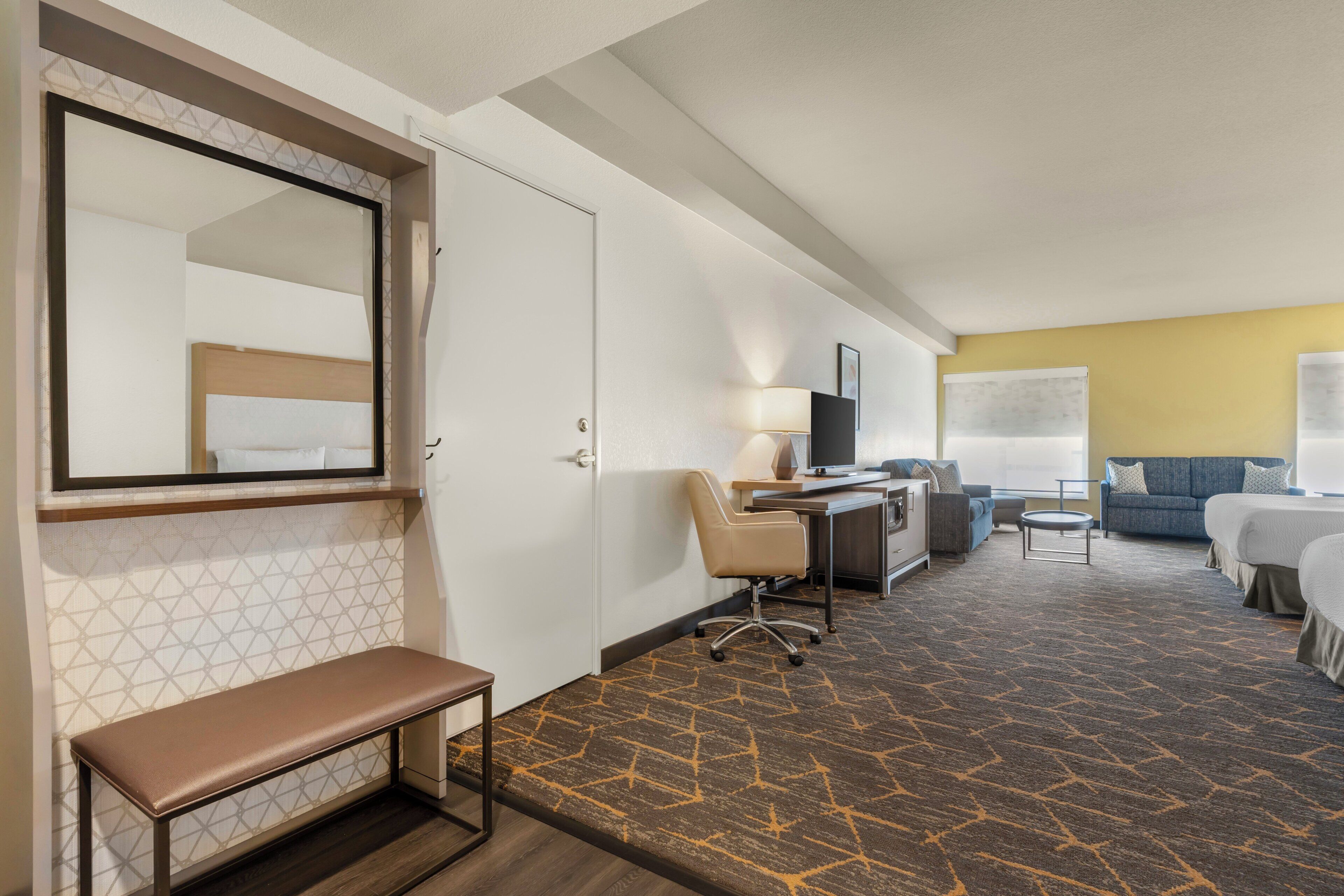 A hotel room with a bed, desk, chair, and a bench.
