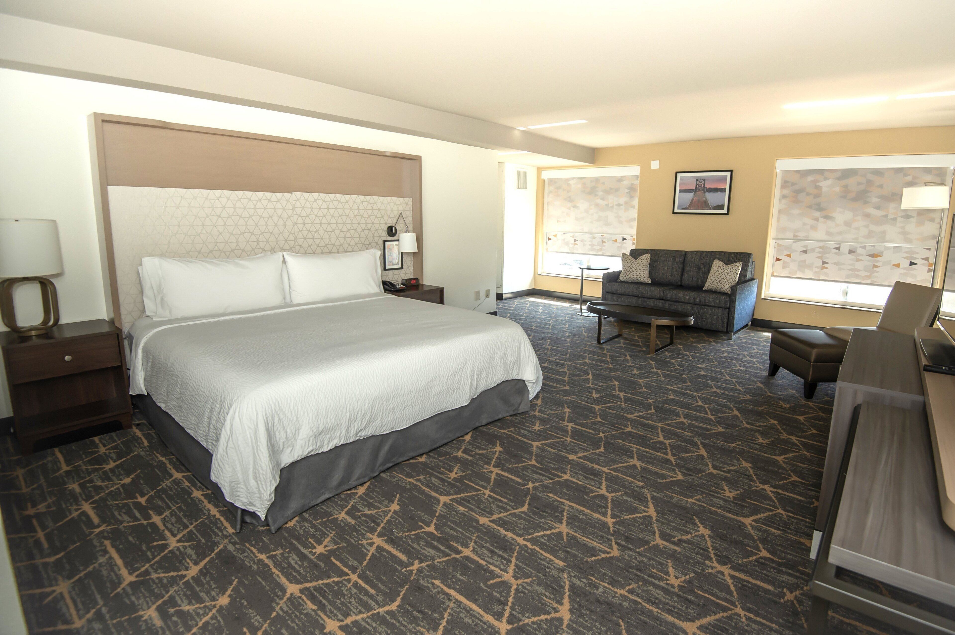 Quarto de hotel com cama grande, sofá, escrivaninha e janela com persianas.
