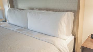 A neatly made bed with white linens, a headboard with a geometric pattern, and a small bedside table with a power outlet.