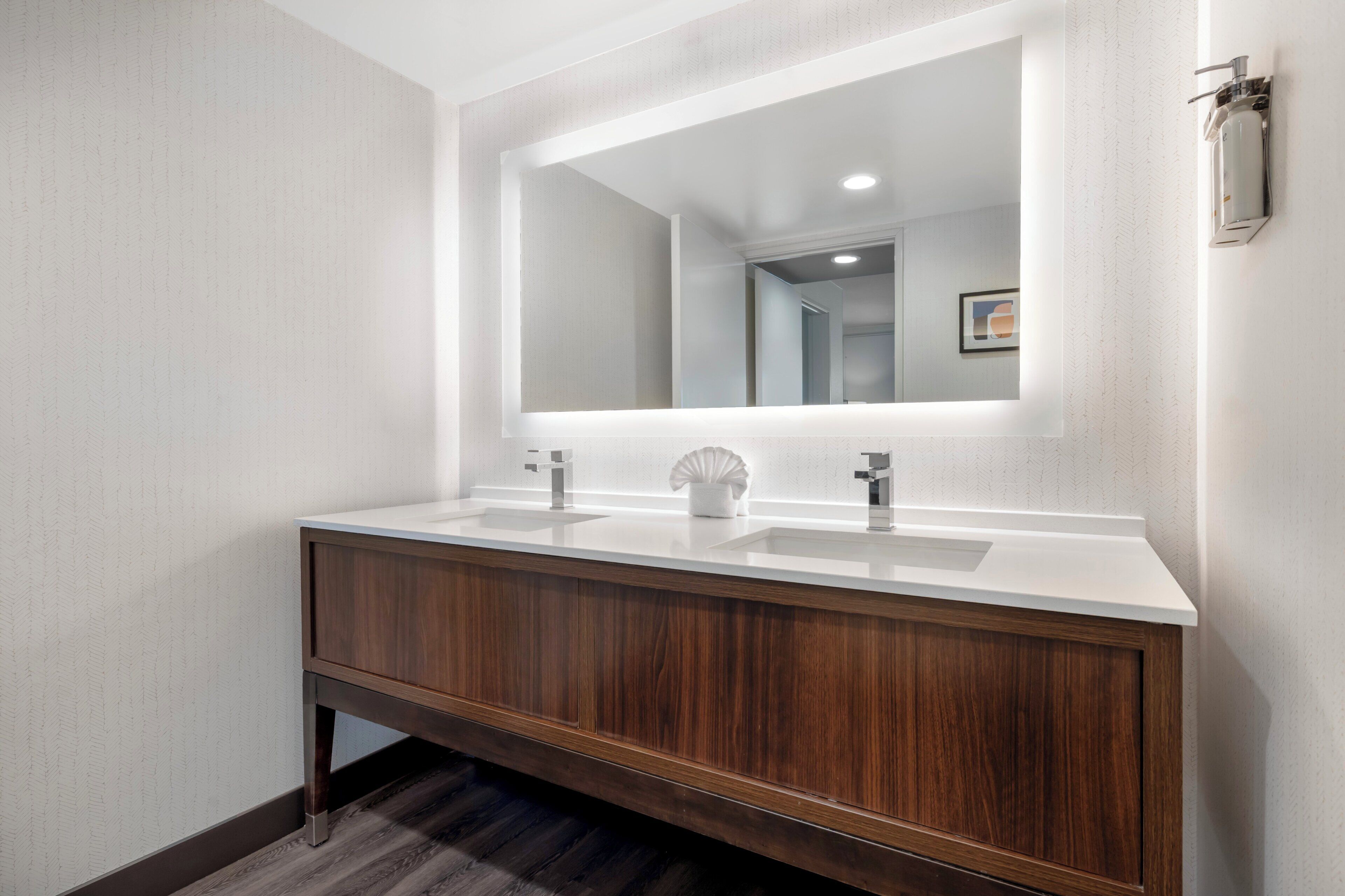 A modern bathroom with a double sink vanity, a large mirror, and a wall-mounted faucet.