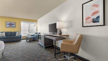 A hotel room with a sofa, a desk, a chair, a television, and a window.