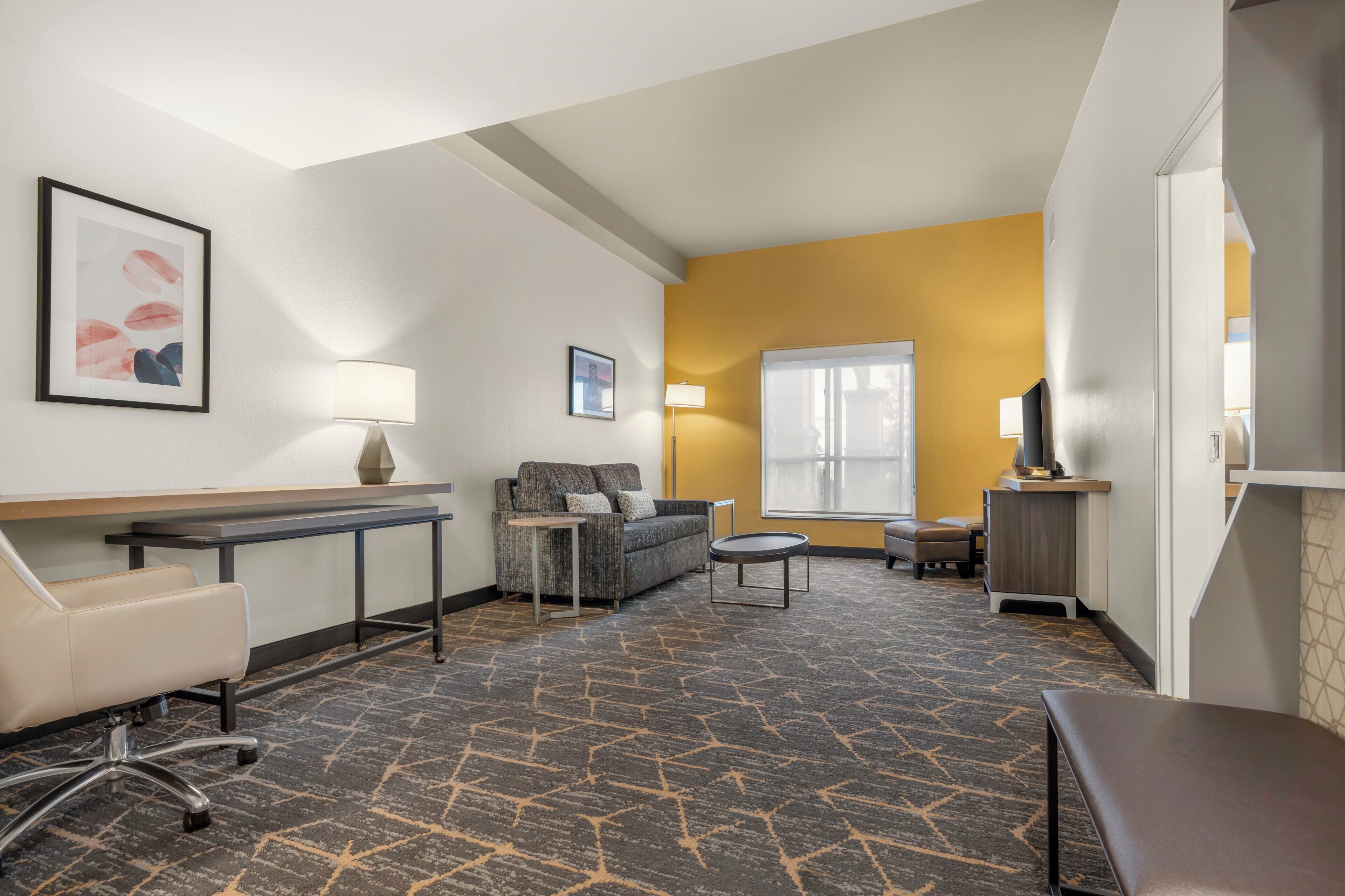 A hotel room with a sofa, a desk, a chair, a small table, and a television.