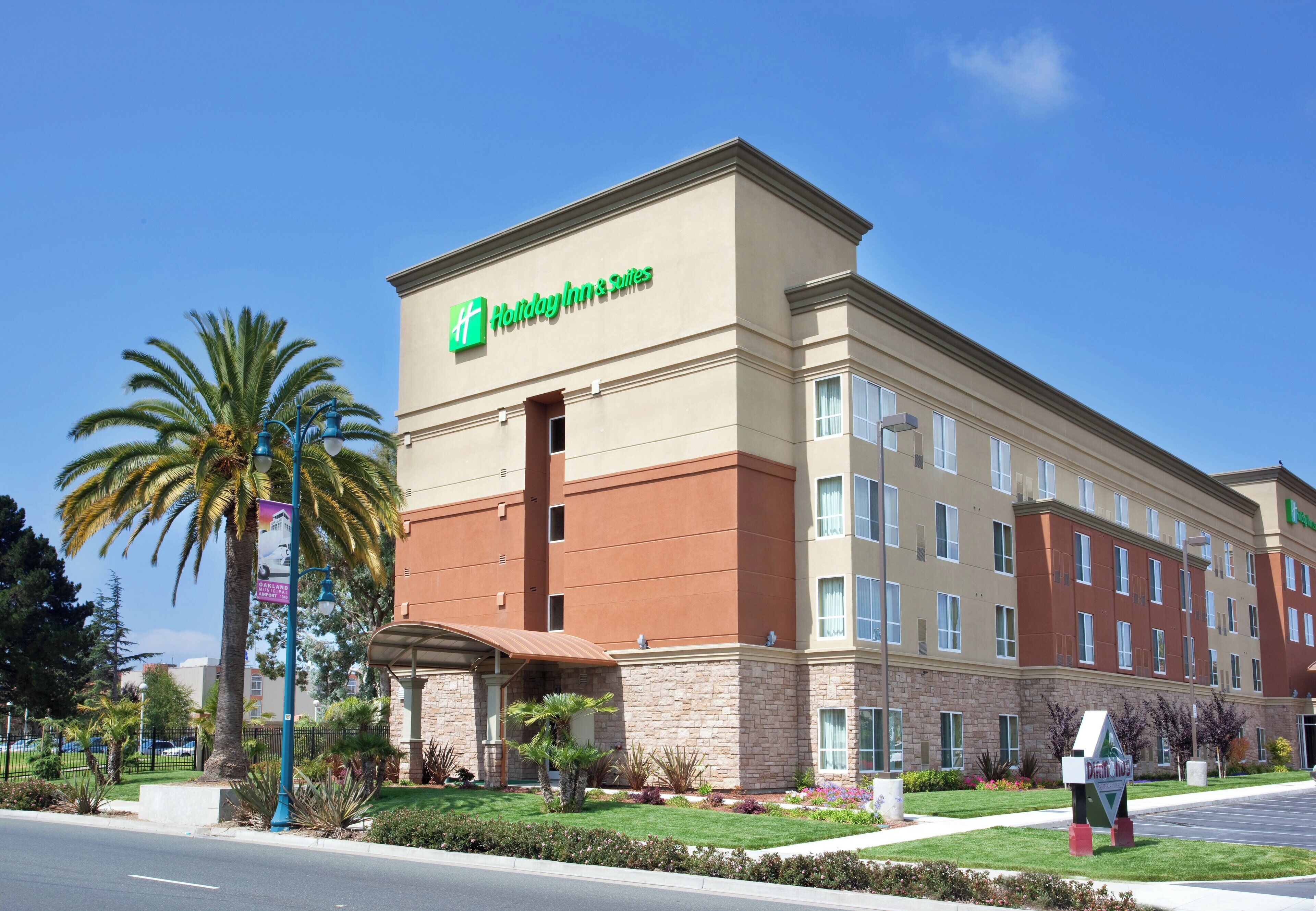 Een Holiday Inn & Suites hotel met een gevel van natuursteen, meerdere ramen en een heldere blauwe lucht.
