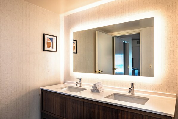 Ein Badezimmer mit zwei Waschbecken, einem großen Spiegel und einem gerahmten Bild an der Wand.