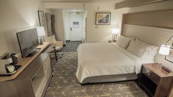 Een hotelkamer met een bed, nachtkastje, bureau met een computer, stoel en een televisie.