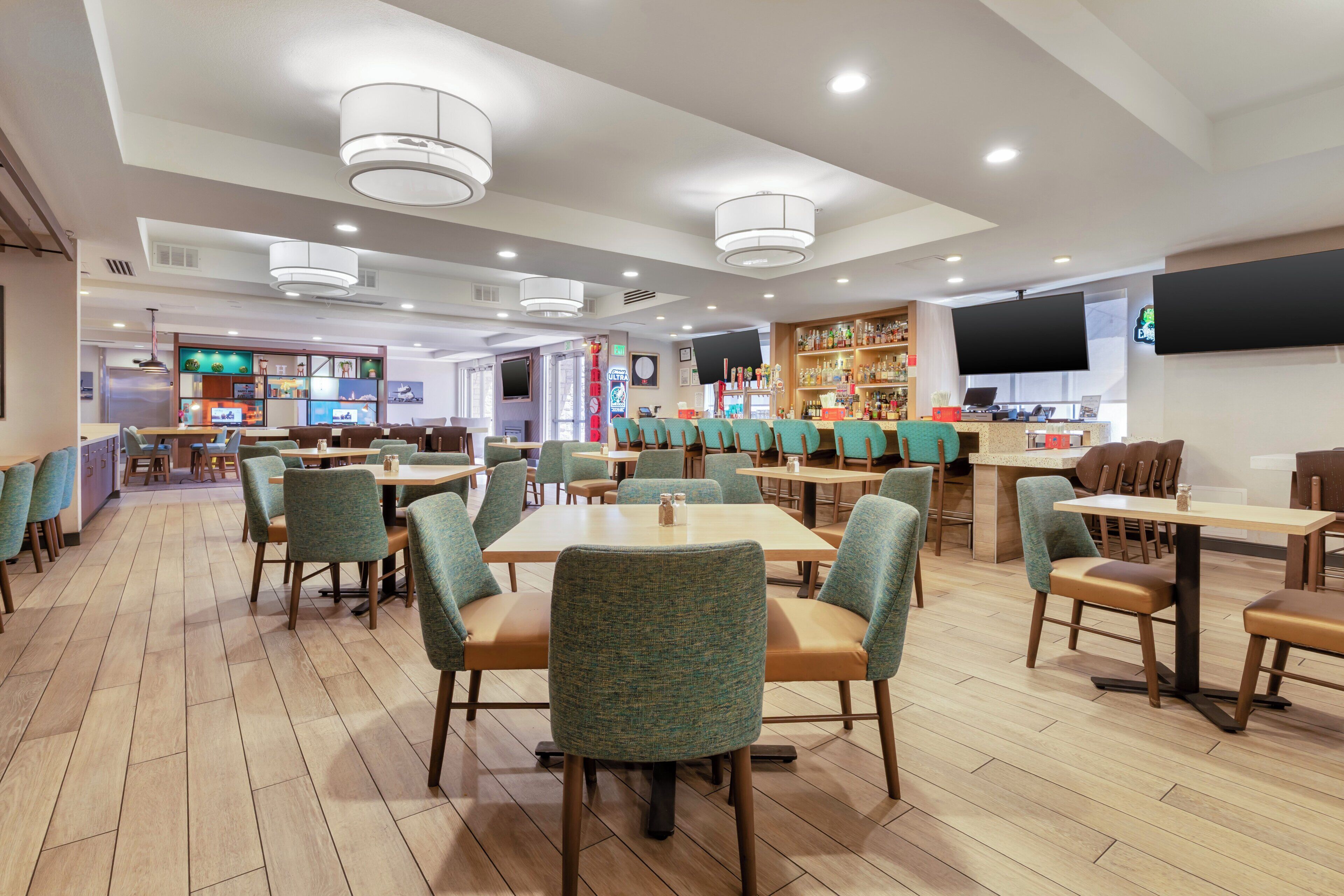 A restaurant with multiple tables and chairs, a bar area, and a television screen mounted on the wall.