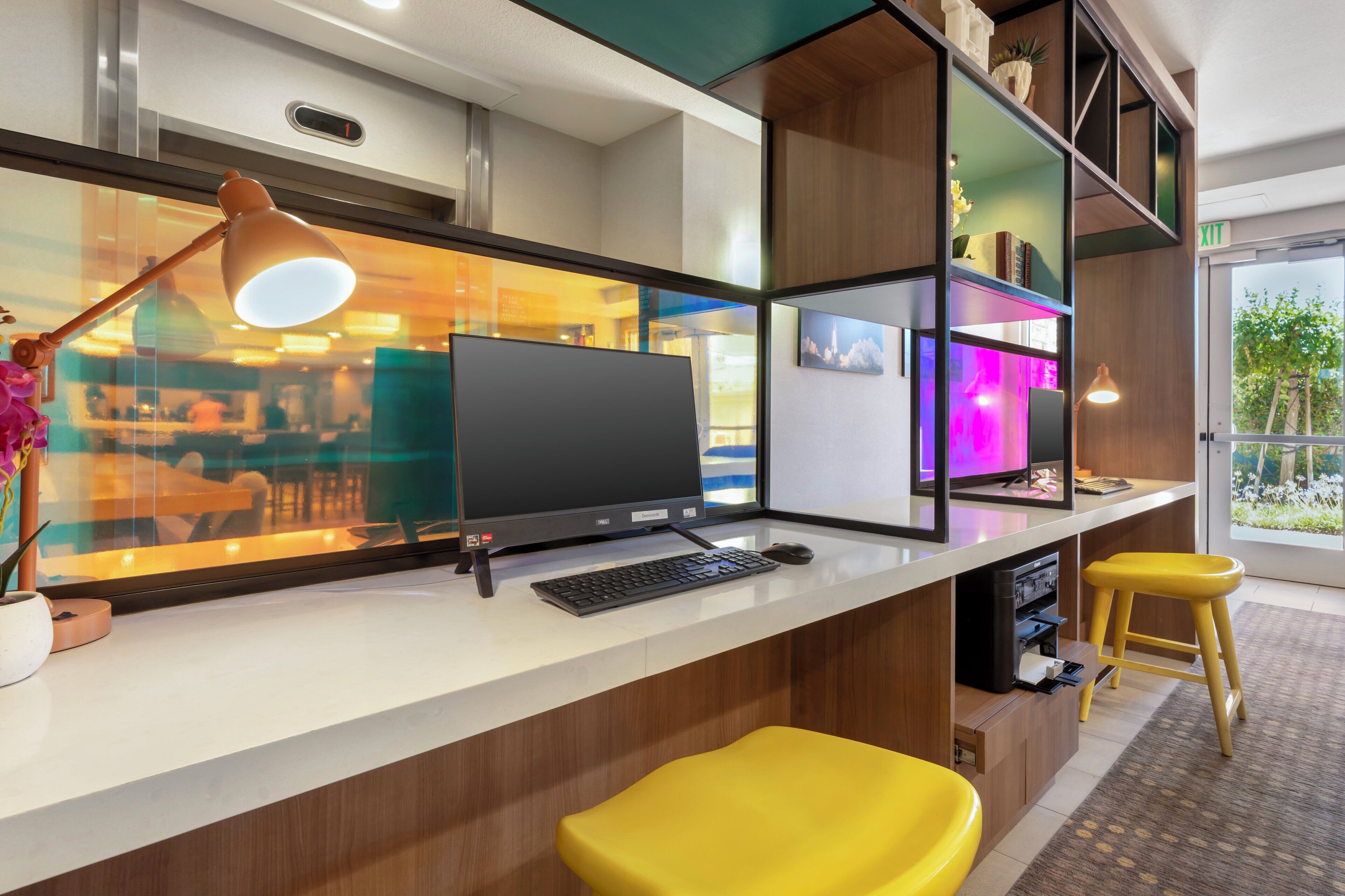 A modern office space with a desk, computer, keyboard, mouse, and a yellow stool.