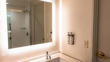 A bathroom with a large mirror, a sink, and a shower visible in the background.