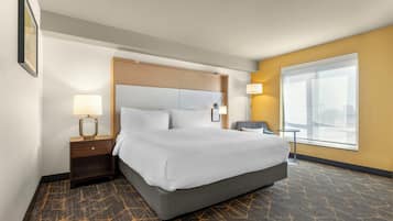 Quarto de hotel com uma cama grande, uma mesa de cabeceira, uma cadeira, uma janela e um abajur.