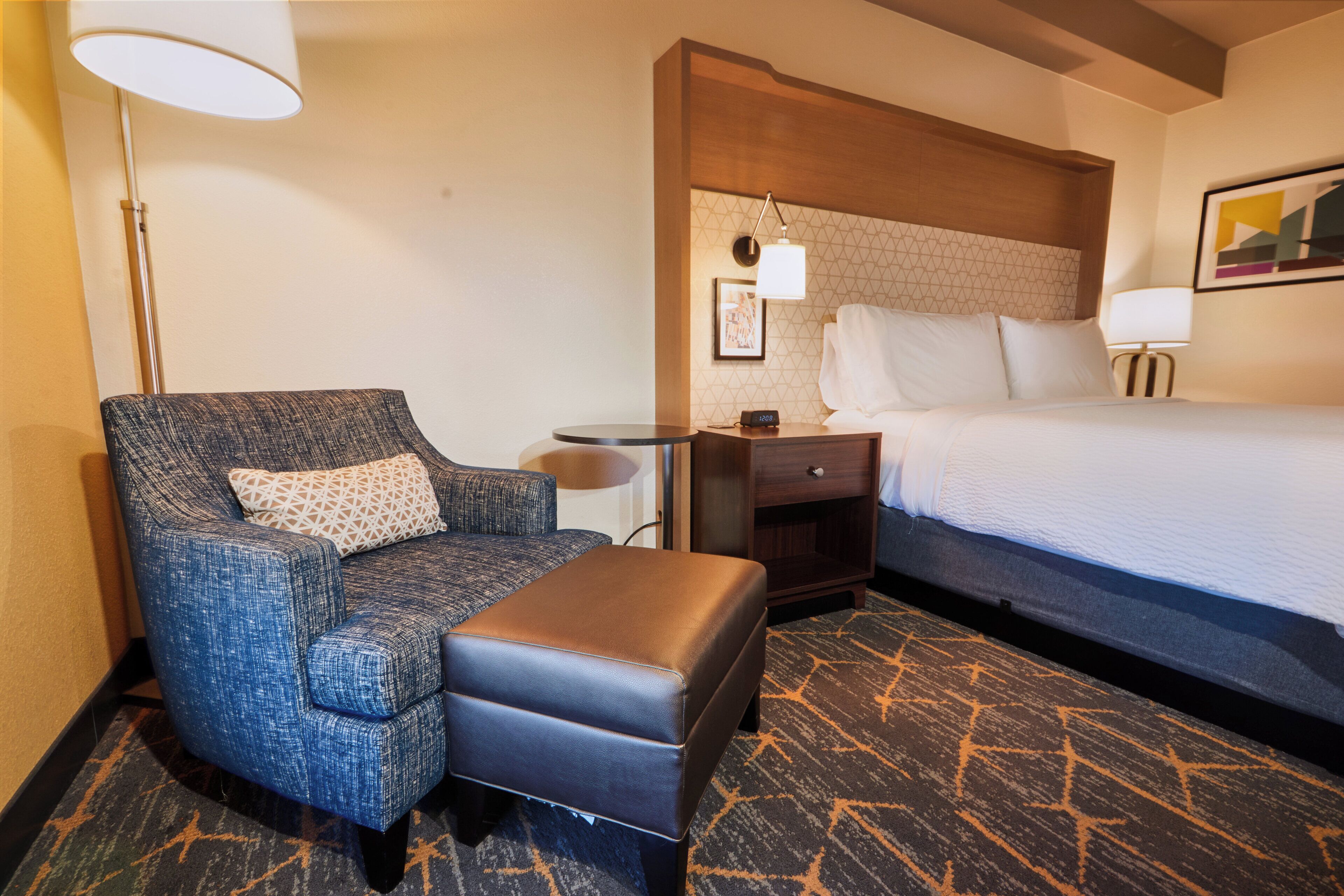 A hotel room with a bed, a sofa, a nightstand, and a lamp.