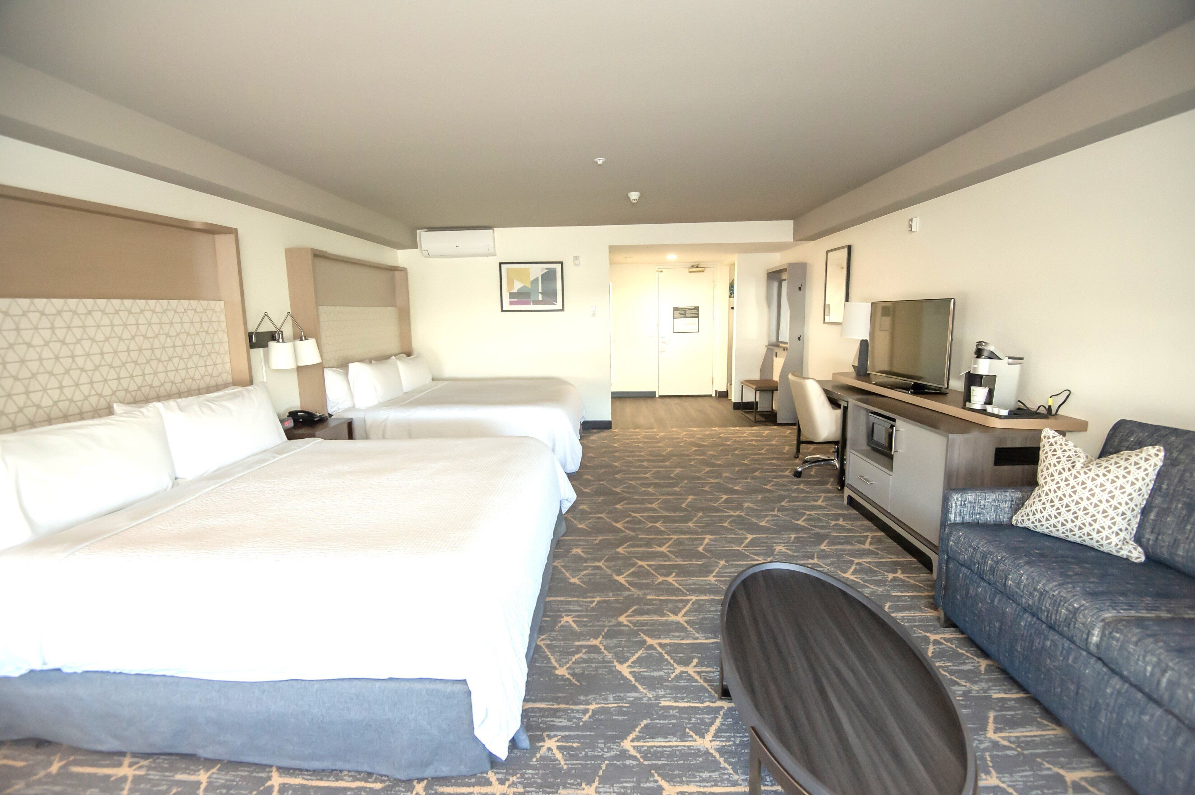 A hotel room with two beds, a sofa, a TV, and a desk with a computer.